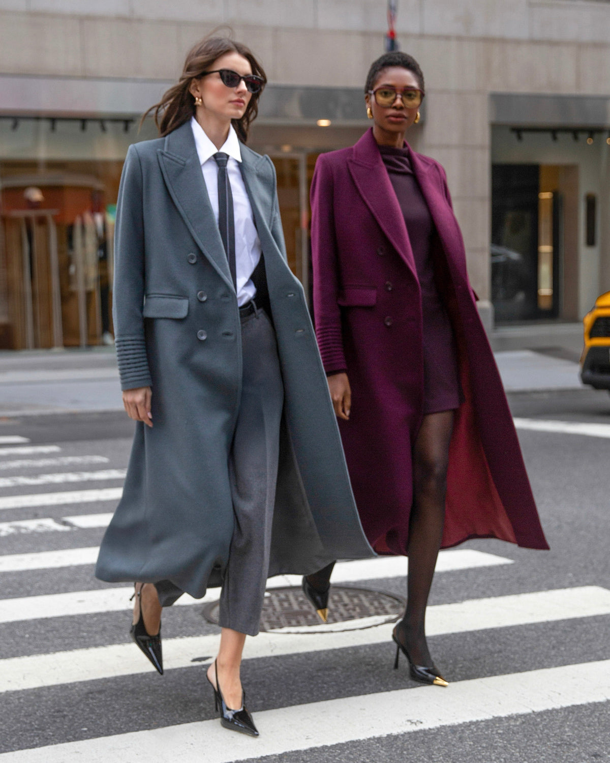 Side view of models wearing Sentaler cherry lacquer & graphite double breasted maxi coat made of baby alpaca wool, with a peak collar, worn buttoned.