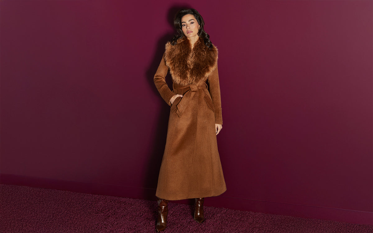Front view of model wearing a  Sentaler caramel maxi coat made of suri alpaca wool, with an alpaca shearling collar, seen belted.