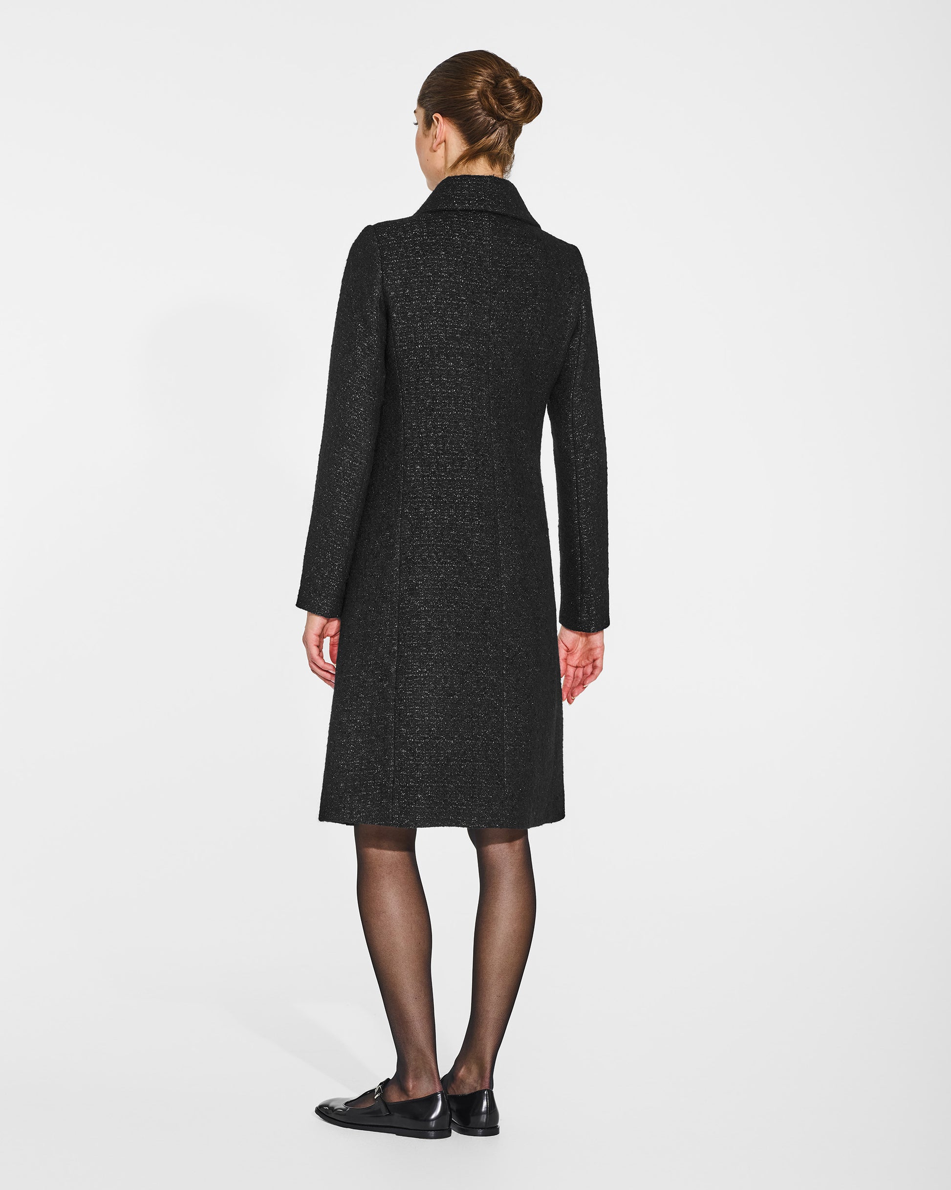 Back view of model in Sentaler black glittered A-line coat with empire waist in tweed suri alpaca, buttoned.