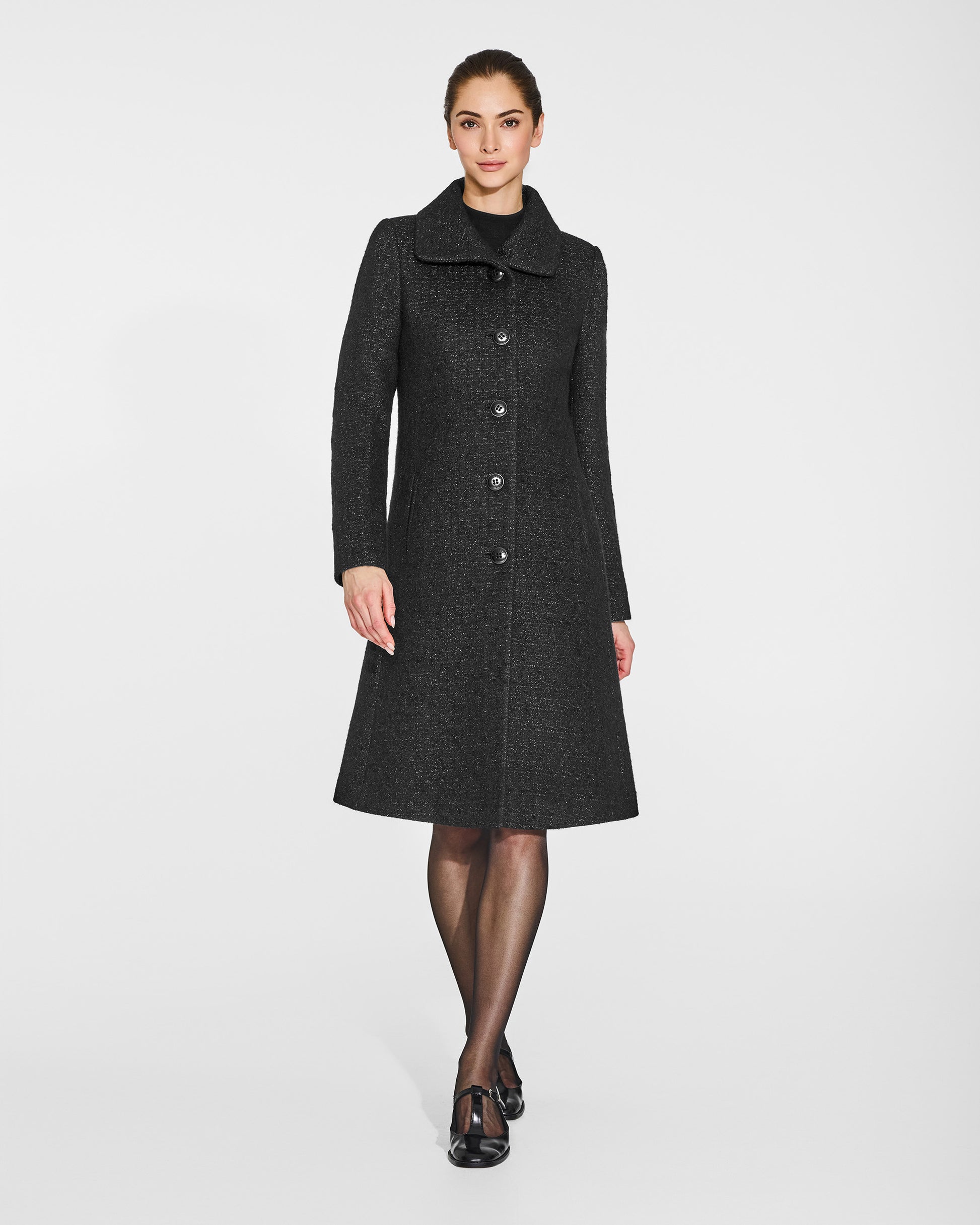 Front view of model in Sentaler black glittered A-line coat with empire waist in tweed suri alpaca, buttoned.