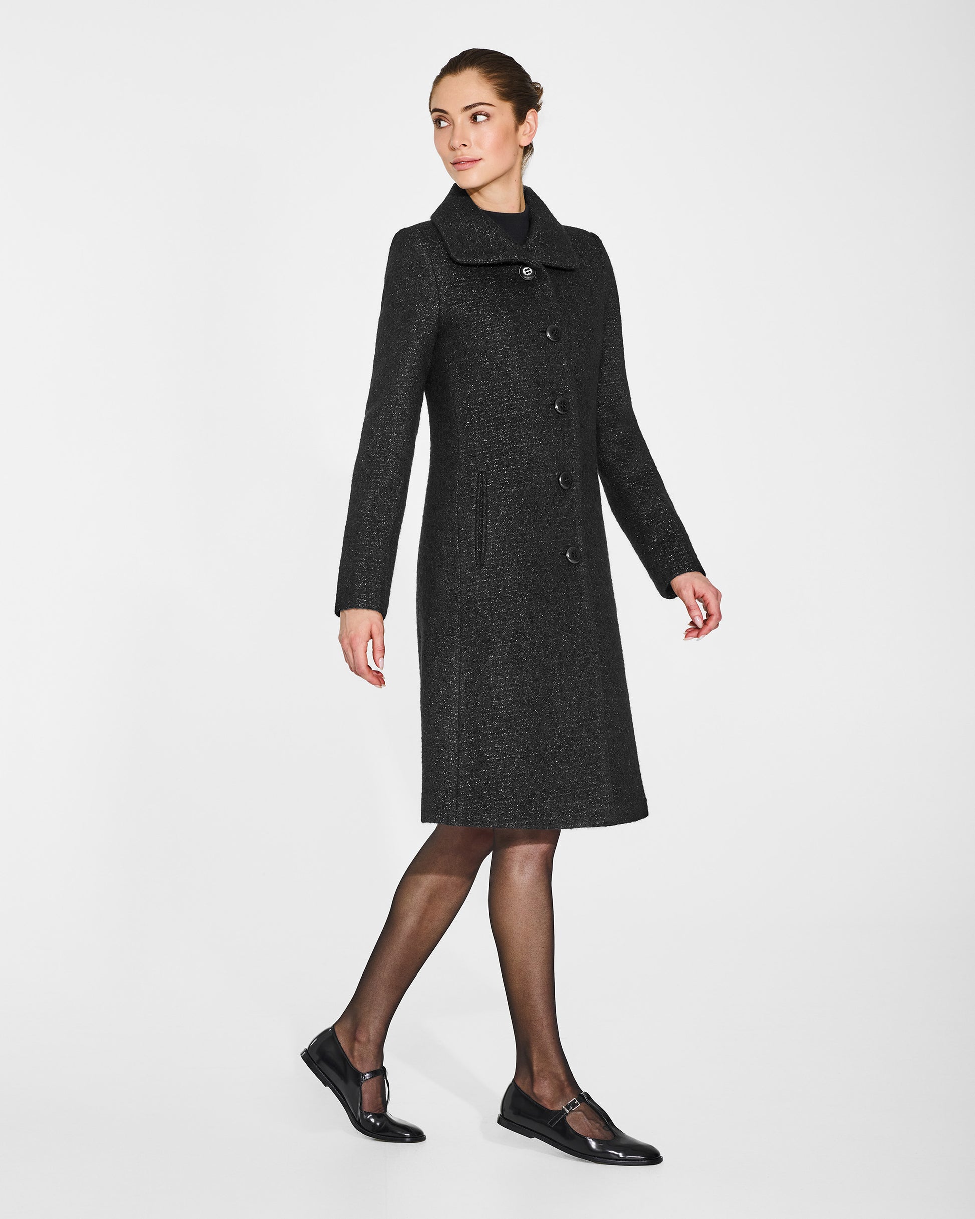 Side view of model in Sentaler black glittered A-line coat with empire waist in tweed suri alpaca, buttoned.