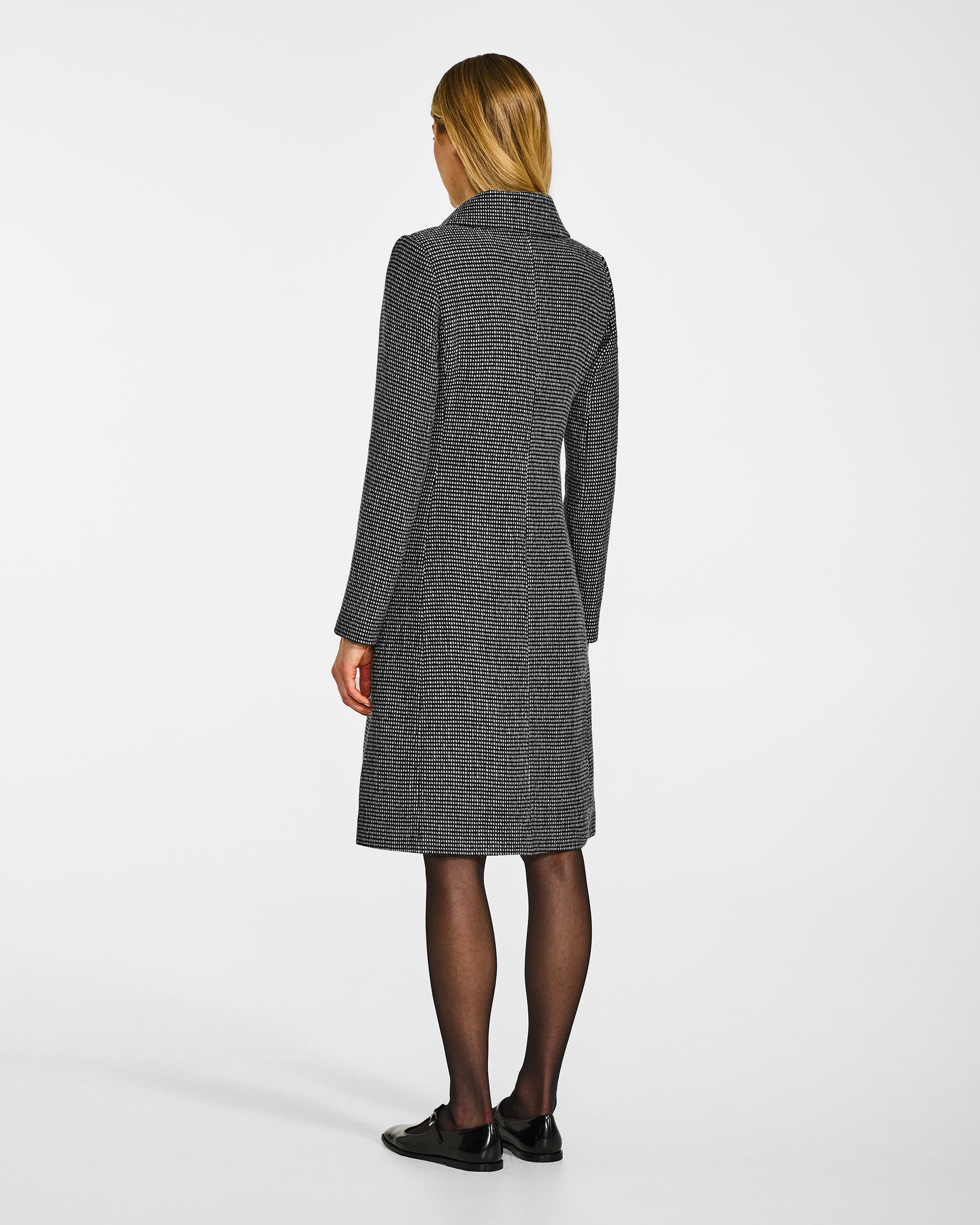 Back view of model wearing a Sentaler black, gold and ivory A-line coat made of tweed suri alpaca wool, worn buttoned.