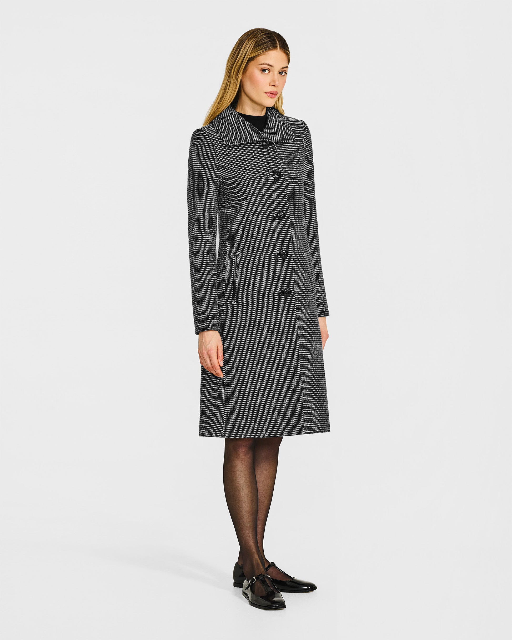 Side view of model wearing a Sentaler black, gold and ivory A-line coat made of tweed suri alpaca wool, worn buttoned.