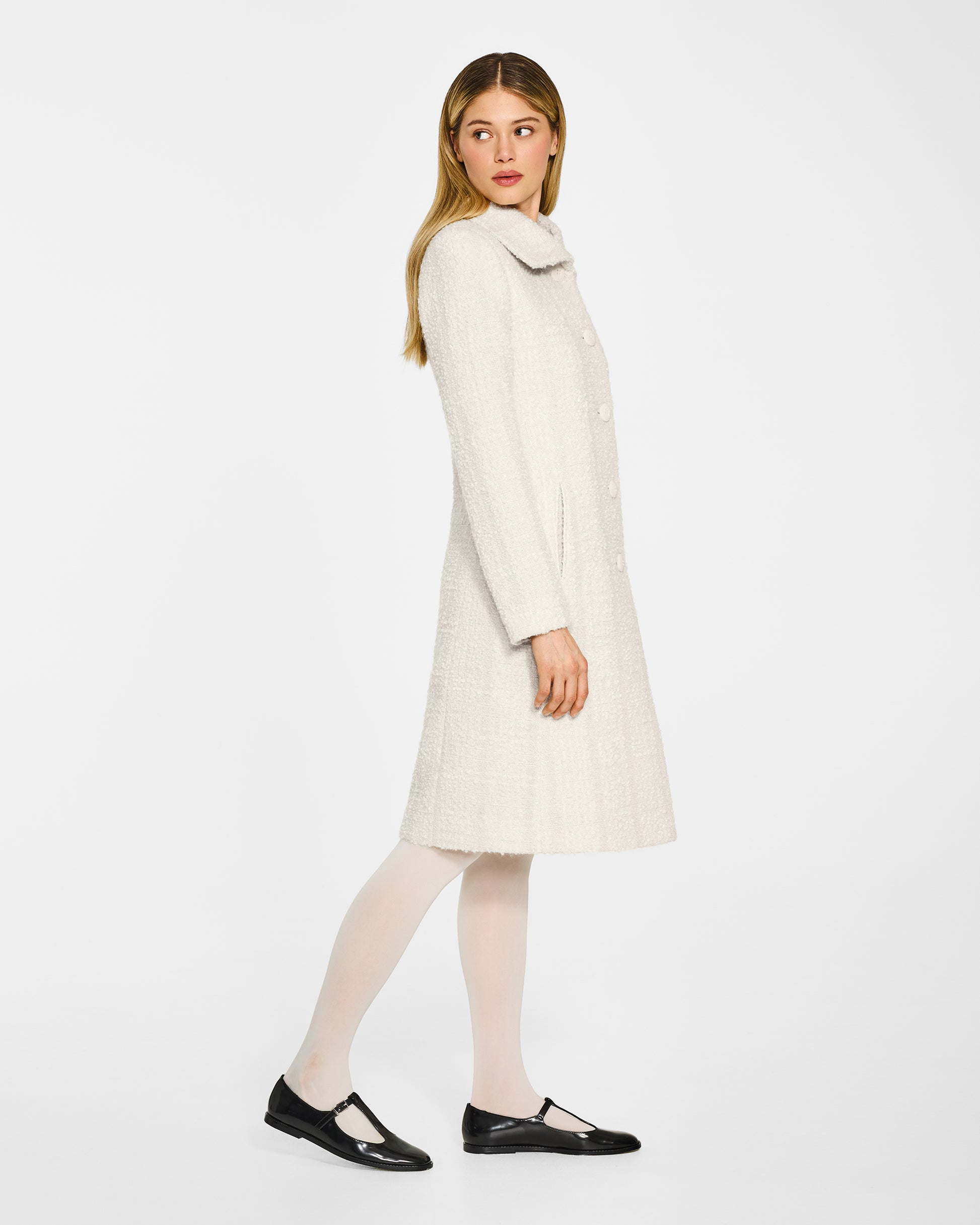 Side view of model wearing a Sentaler ivory glittered A-line coat made of tweed suri alpaca wool, worn buttoned.