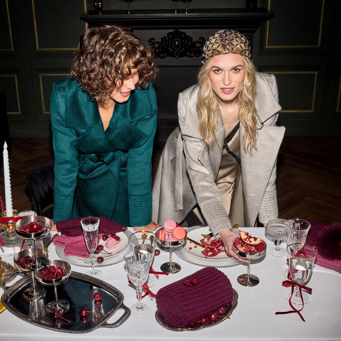 Front view of models wearing Sentaler sand and emerald maxi coats made of suri alpaca wool, with a notched collar, worn belted.