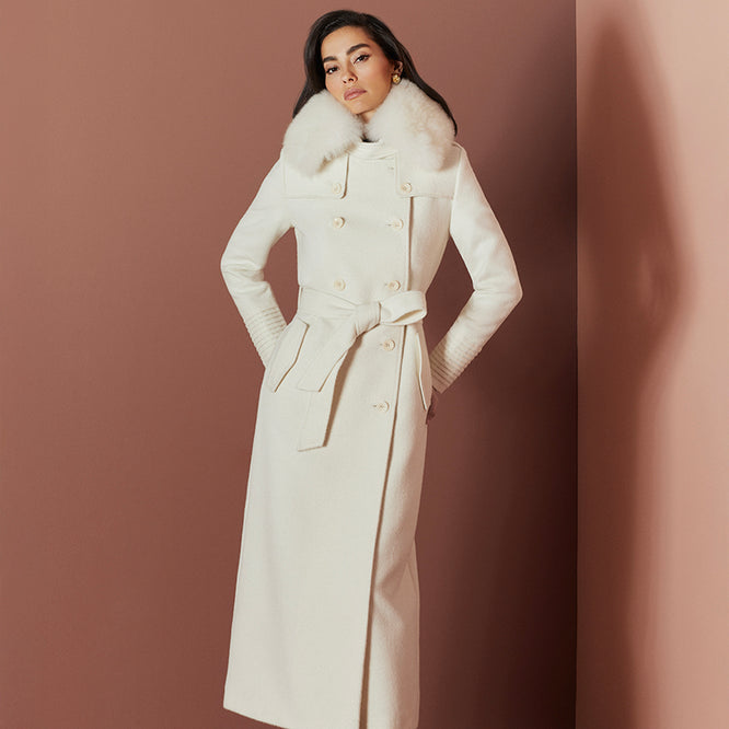 Front view of model in Sentaler maxi ivory trench coat made of baby alpaca wool with shearling collar, buttoned and belted.