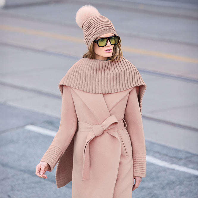 Woman wearing a pink coat with a matching hat and scarf on a road background.