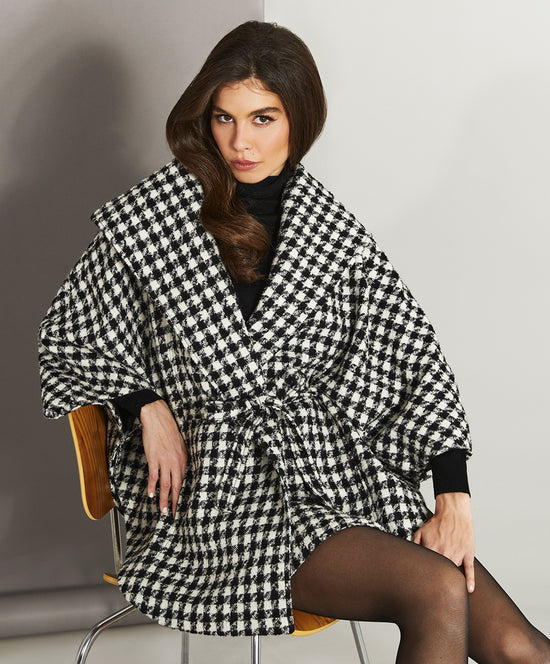 Sentaler Tweed Black and White Houndstooth Cape in Tweed Suri Alpaca wool. Seen from front on female model sitting on a wooden chair.