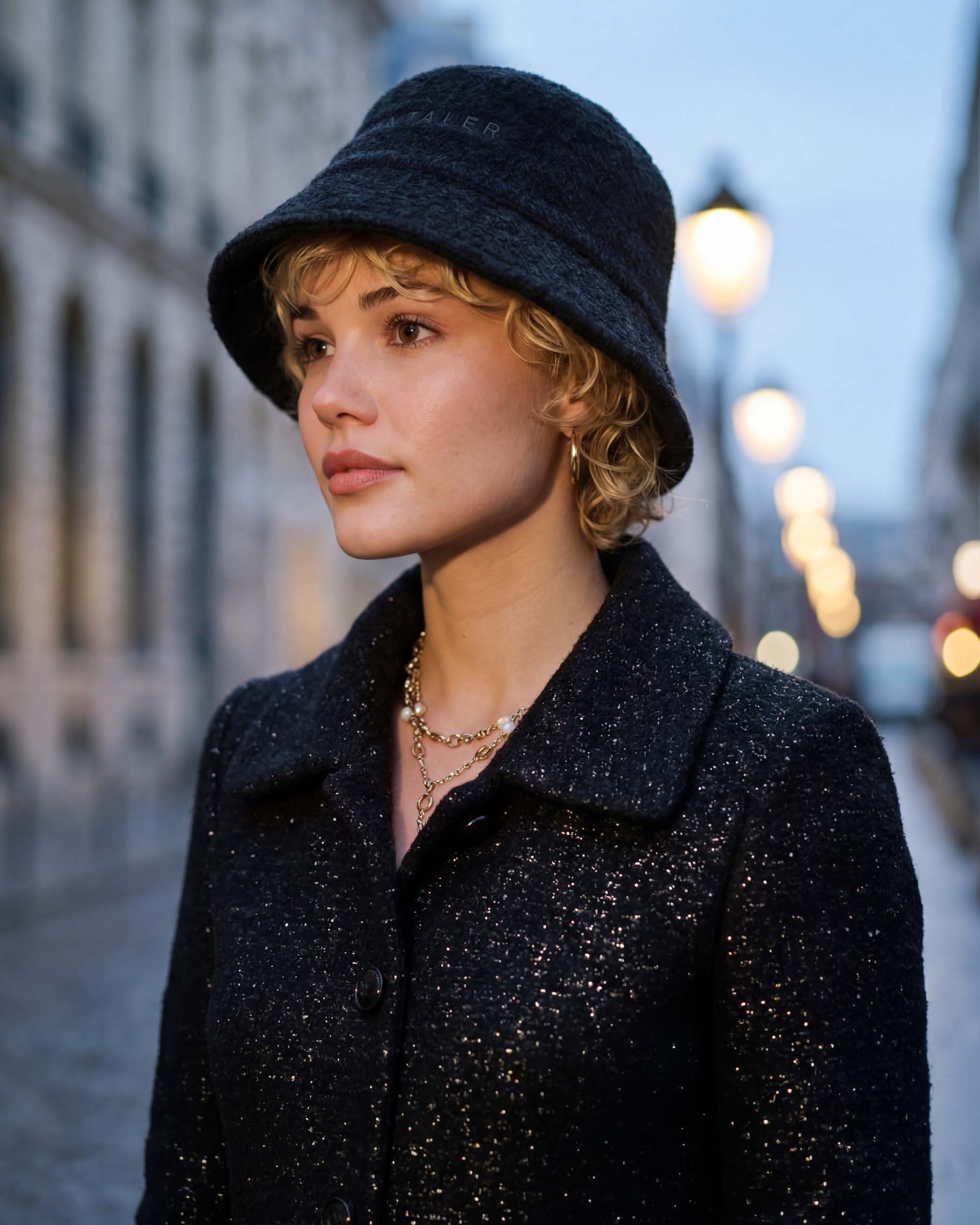 Front view of model wearing a Sentaler black glittered A-line coat made of tweed suri alpaca wool, worn buttoned.