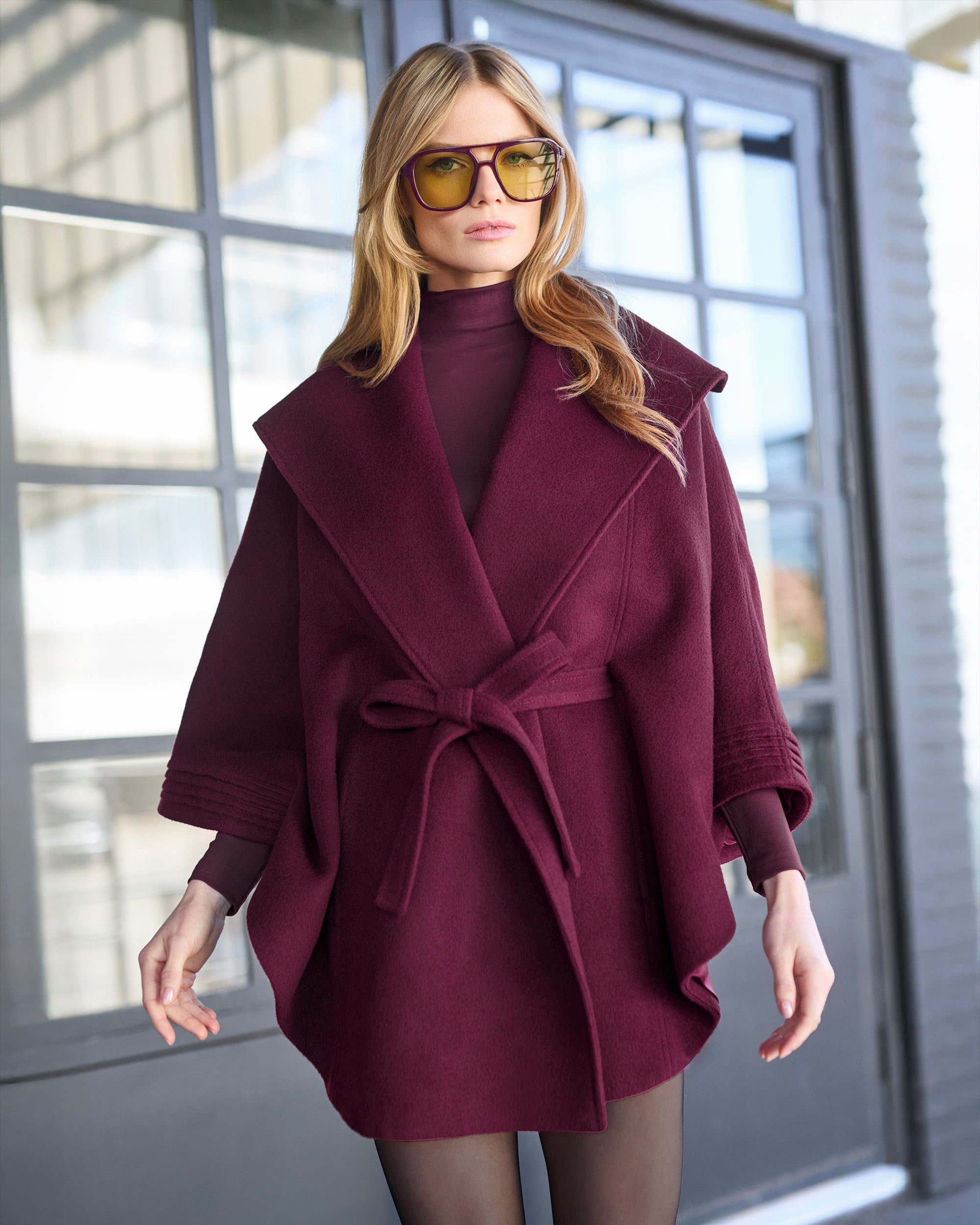 Front close up view of model wearing a Sentaler cherry lacquer cape made of baby alpaca wool, with a shawl collar, worn belted with matching cherry lacquer classic baby alpaca scarf.