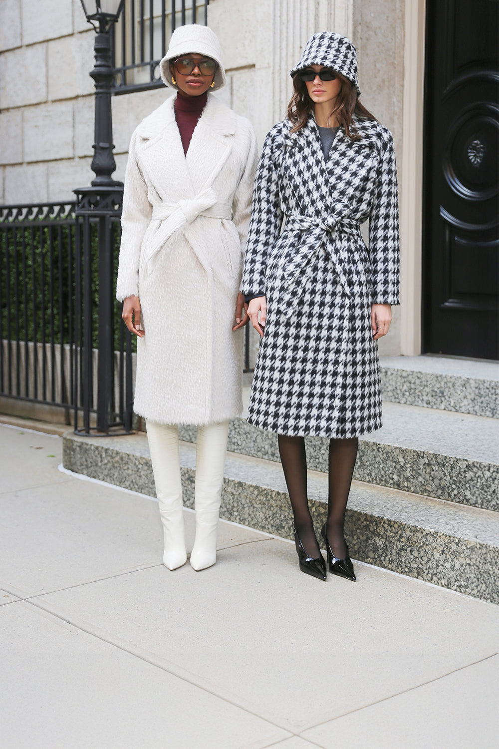 Front view of models wearing a Sentaler oat & black & white houndstooth notched collar coat made of textured suri alpaca wool, with raglan sleeves, worn belted.