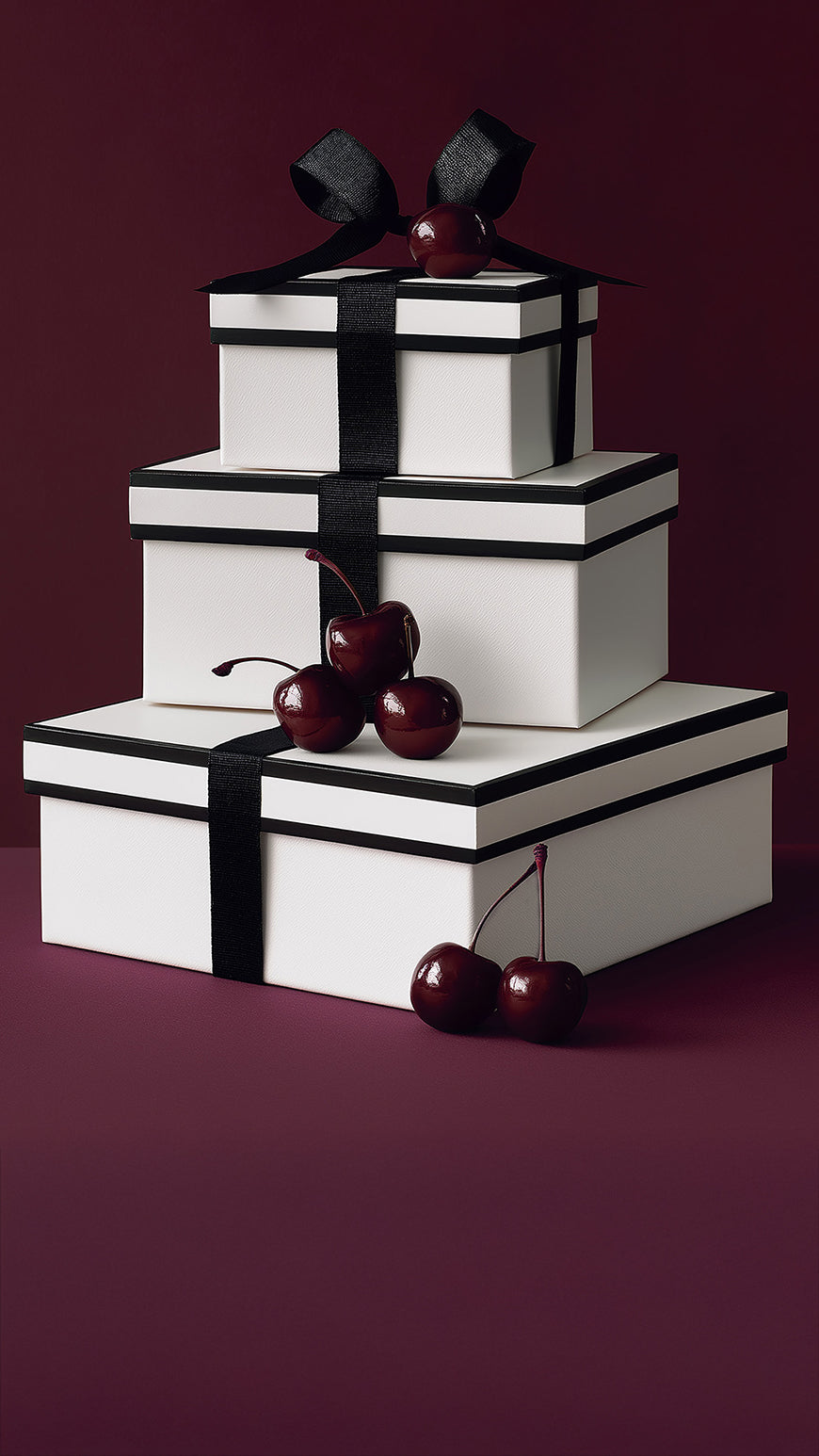 Three white gift boxes wrapped in black ribbon and accented with deep red cherries, styled against a rich burgundy backdrop for the SENTALER Gift Guide.