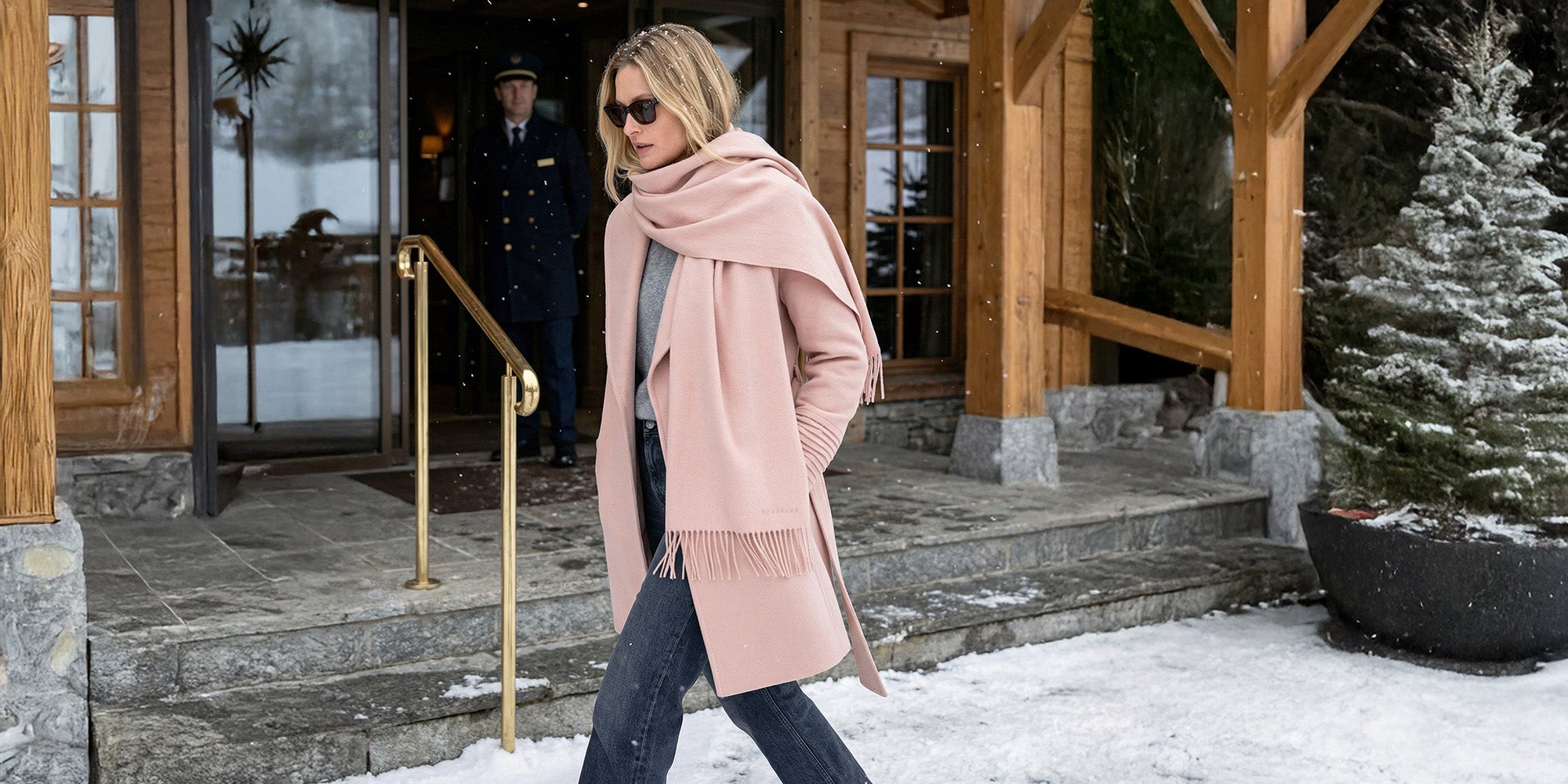 Front view of model wearing a Sentaler mid length blush pink coat made of baby alpaca wool, with a shawl collar, worn belted.