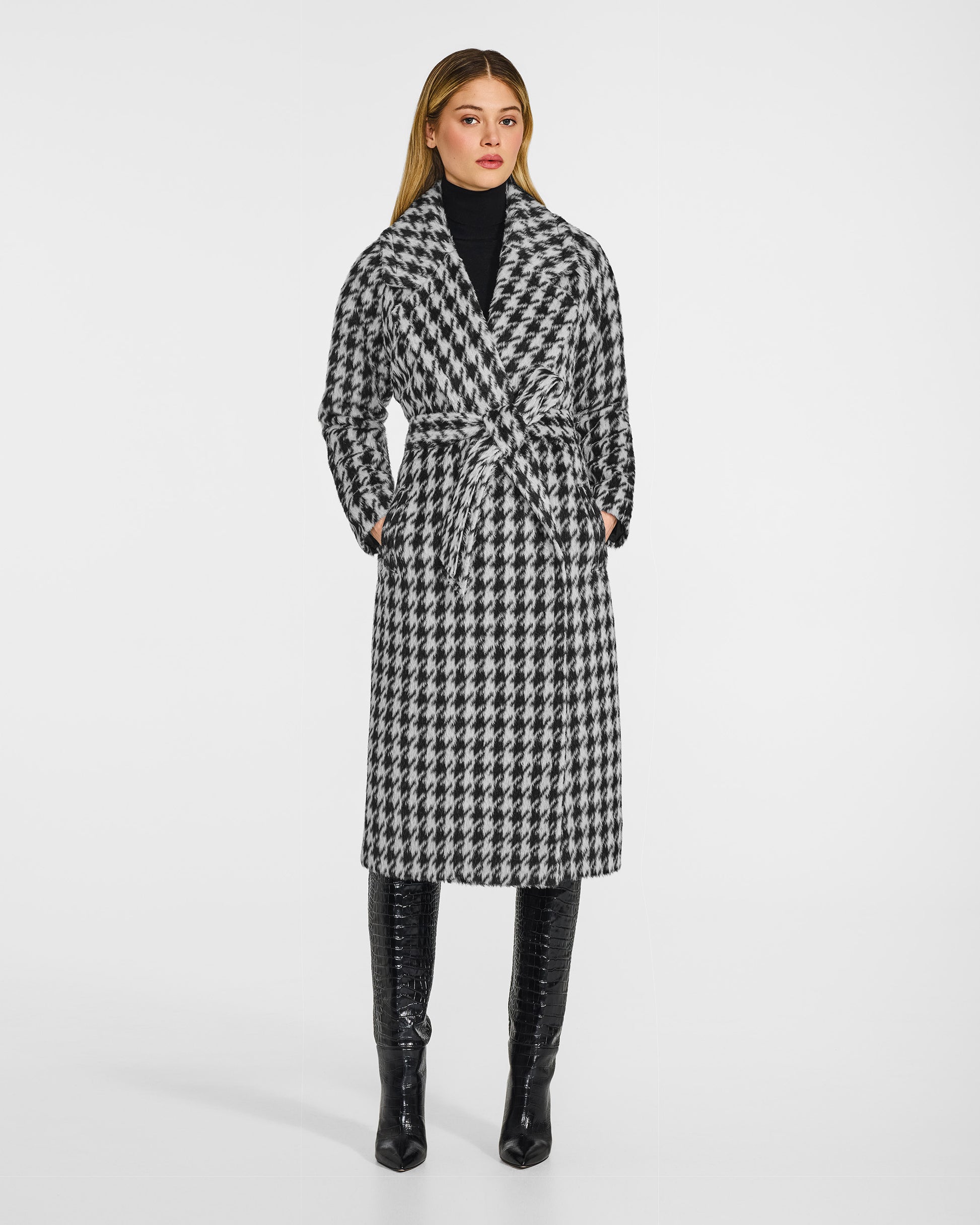 Front view of model wearing a Sentaler black and white houndstooth coat made of suri alpaca wool, with raglan sleeves, worn belted. 
