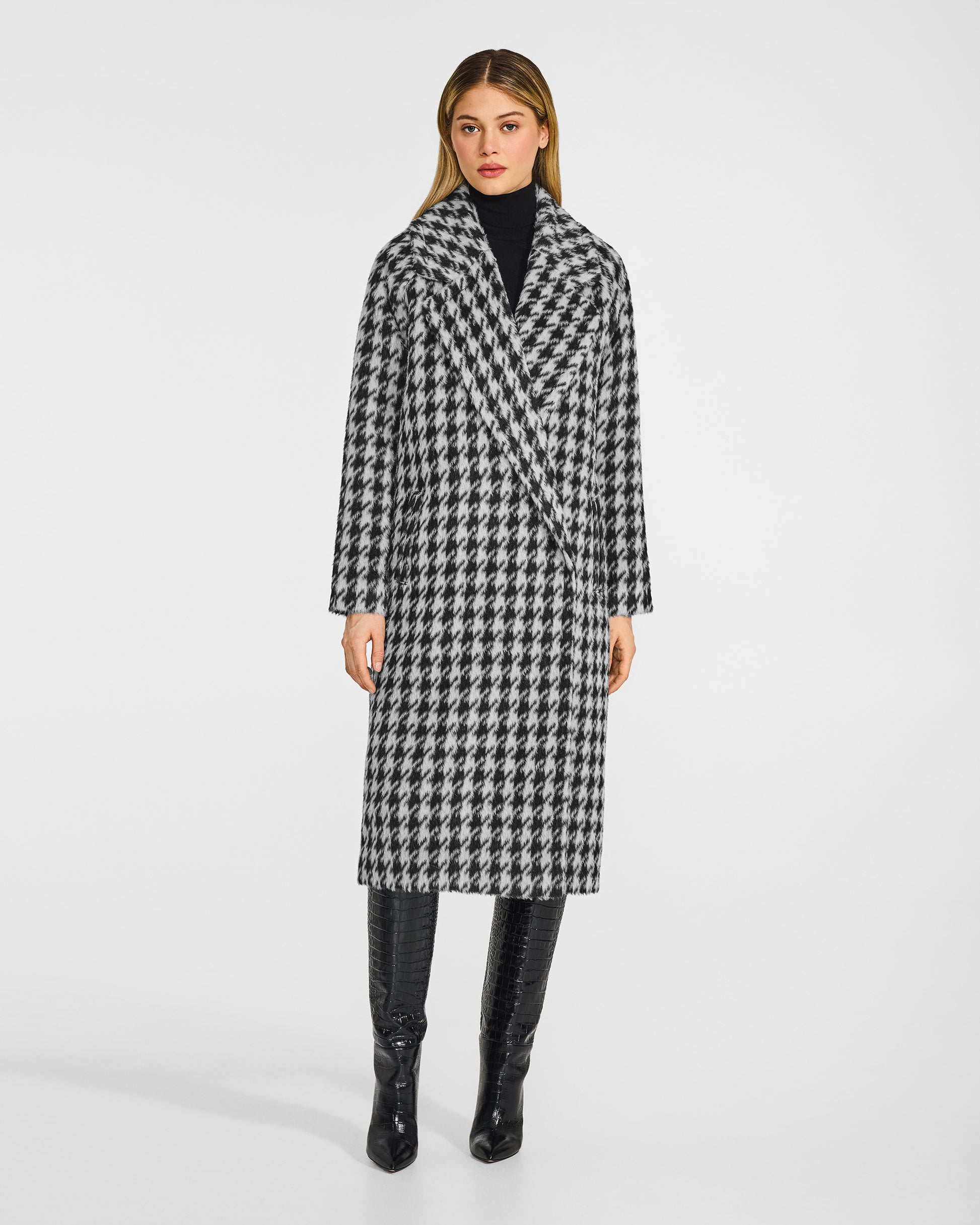 Front view of model wearing a Sentaler black and white houndstooth coat made of suri alpaca wool, with raglan sleeves, worn buttoned.