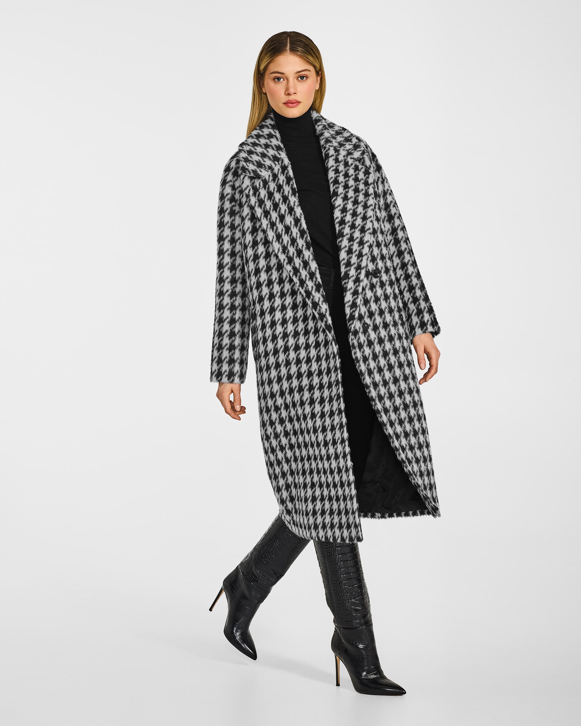 Side view of model wearing a Sentaler black and white houndstooth coat made of suri alpaca wool, with raglan sleeves, worn open.