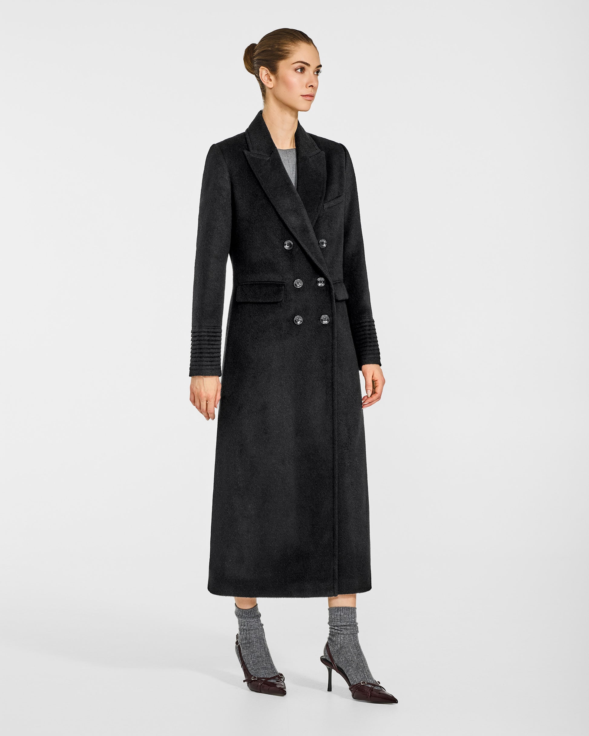 Side view of model wearing a Sentaler black double breasted maxi coat made of baby alpaca wool, with a peak collar, worn buttoned.
