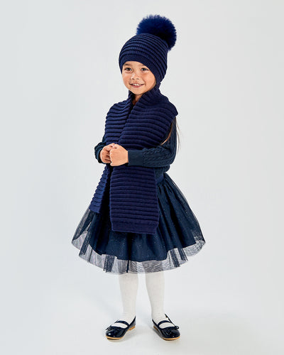 Sentaler Kids Ribbed Navy Scarf (4-5 Years) and Kids Ribbed Navy Hat with Fur Pompon (4-5 Years) in Baby Alpaca yarn. Seen from front on girl model.