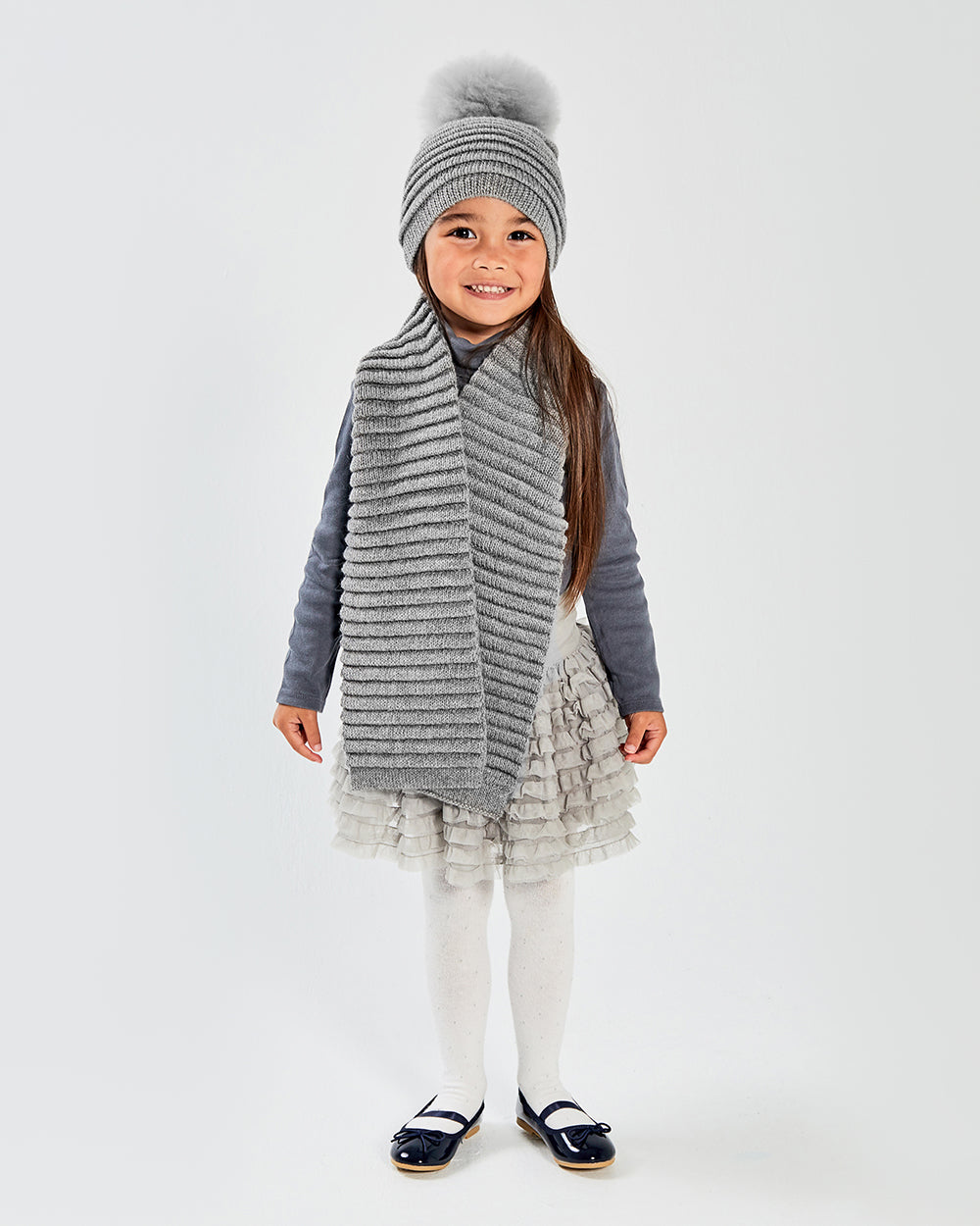 Sentaler Kids Ribbed Grey Scarf (4-5 Years) and Kids Ribbed Grey Hat with Fur Pompon (4-5 Years) in Baby Alpaca yarn. Seen from front on girl model.