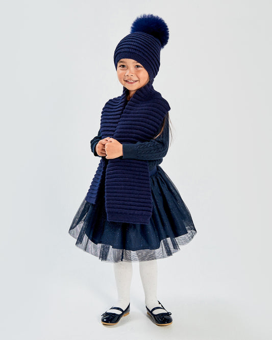 Sentaler Kids Ribbed Navy Scarf (1-5 Years) and Kids Ribbed Navy Hat with Fur Pompon (1-5 Years) in Baby Alpaca yarn. Seen from front on girl model.