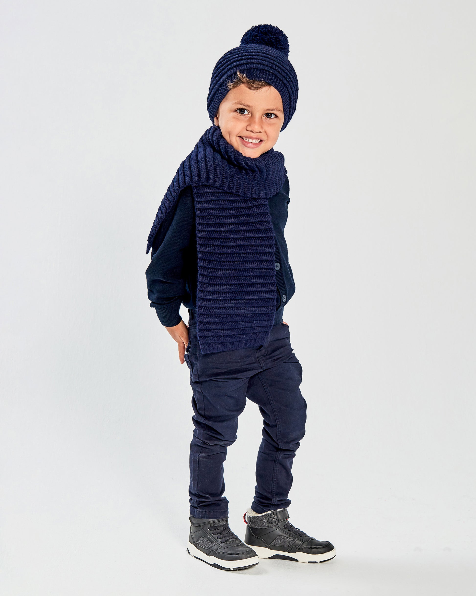 Sentaler Kids Ribbed Navy Hat with Knit Pompon (1-5 Years) and Kids Ribbed Navy Scarf (1-5 Years) in Baby Alpaca yarn. Seen from side on boy model.