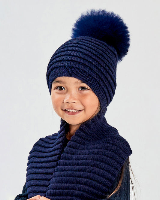 Sentaler Kids Ribbed Navy Hat with Fur Pompon (1-5 Years) and Kids Ribbed Navy Scarf (1-5 Years) in Baby Alpaca yarn. Seen from front close up on girl model.