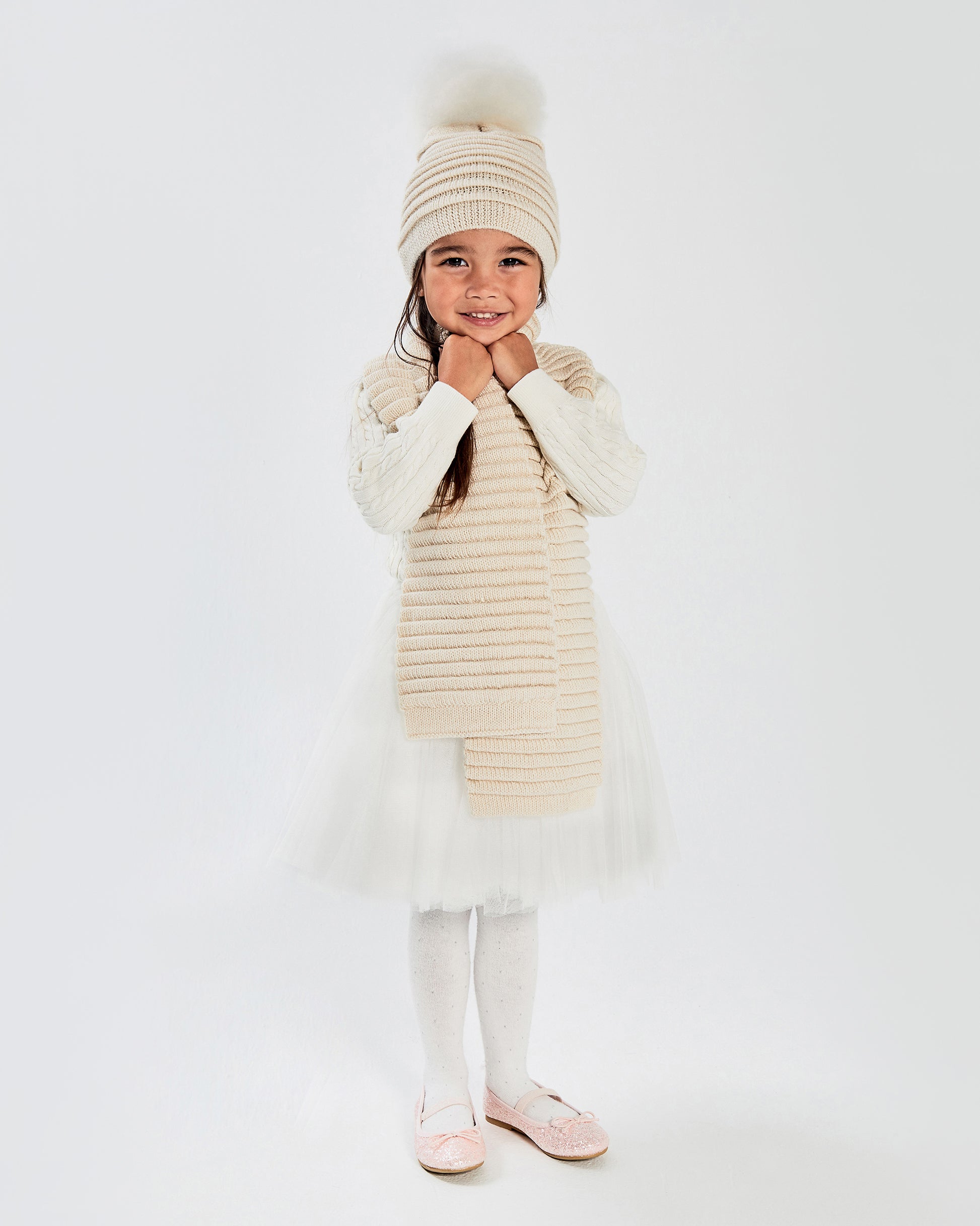 Sentaler Kids Ribbed Ivory Hat with Fur Pompon (1-5 Years) and Kids Ribbed Ivory Scarf (1-5 Years) in Baby Alpaca yarn. Seen from front on girl model.