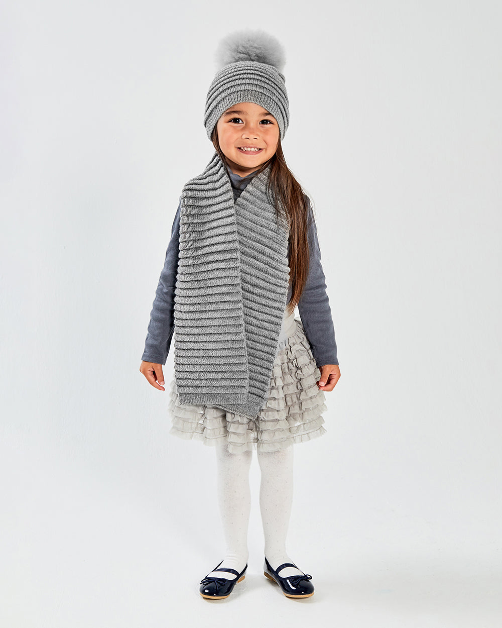 Sentaler Kids Ribbed Grey Hat with Fur Pompon (4-5 Years) and Kids Ribbed Grey Scarf (4-5 Years) in Baby Alpaca yarn. Seen from front on girl model.