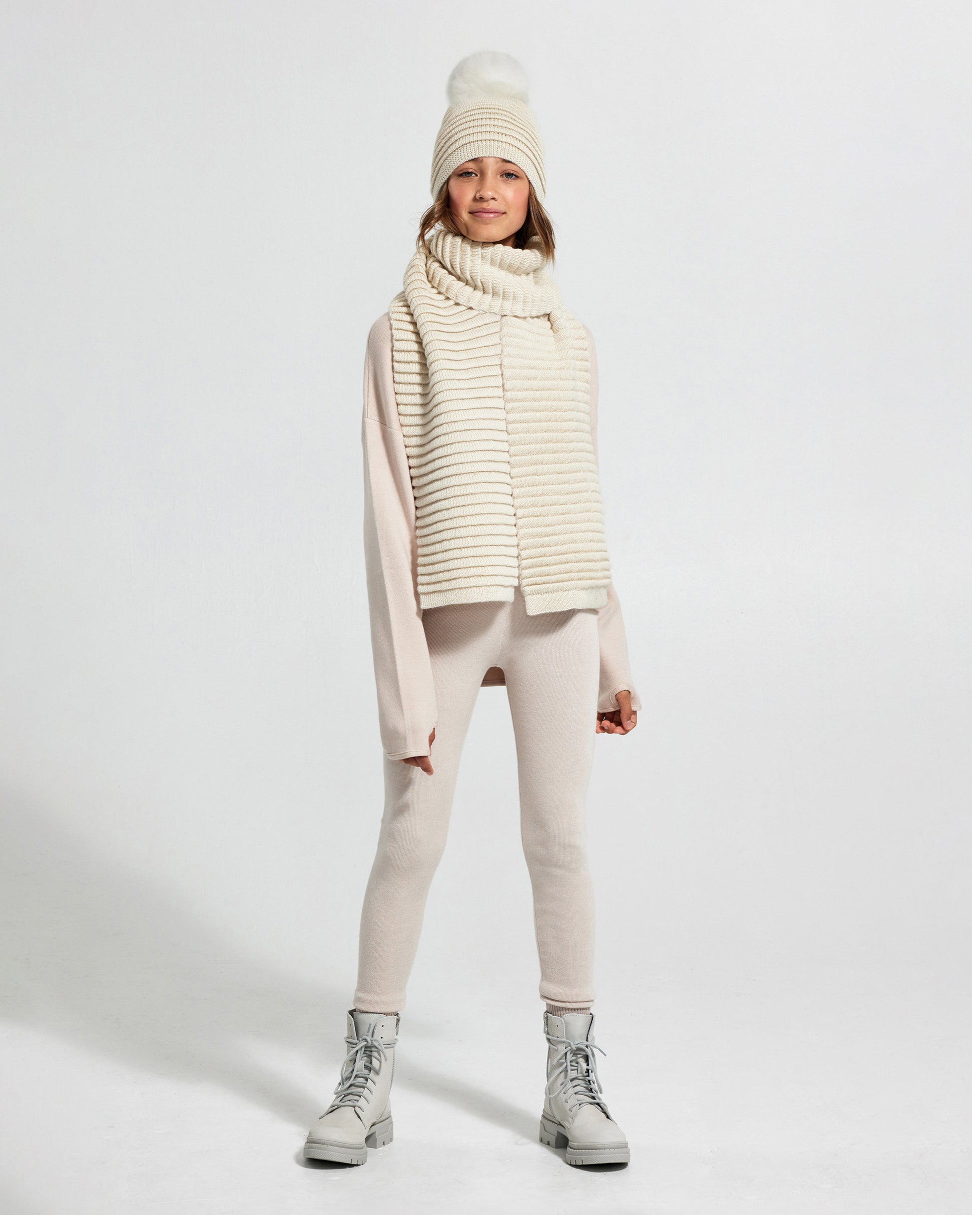Sentaler Kids Ribbed IvoryScarf (6-14 Years) and Kids Ribbed Ivory Hat with Fur Pompon (6-14 Years) in Baby Alpaca yarn. Seen from front on girl model.