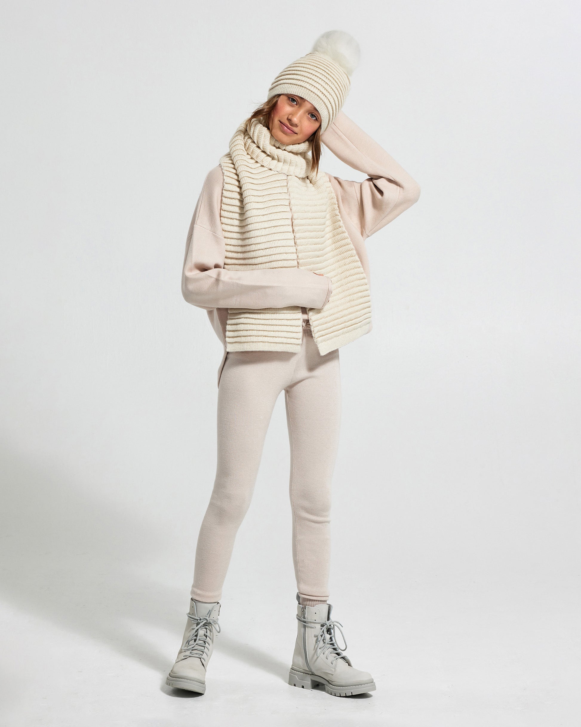 Sentaler Kids Ribbed IvoryScarf (6-14 Years) and Kids Ribbed Ivory Hat with Fur Pompon (6-14 Years) in Baby Alpaca yarn. Seen from front on girl model.