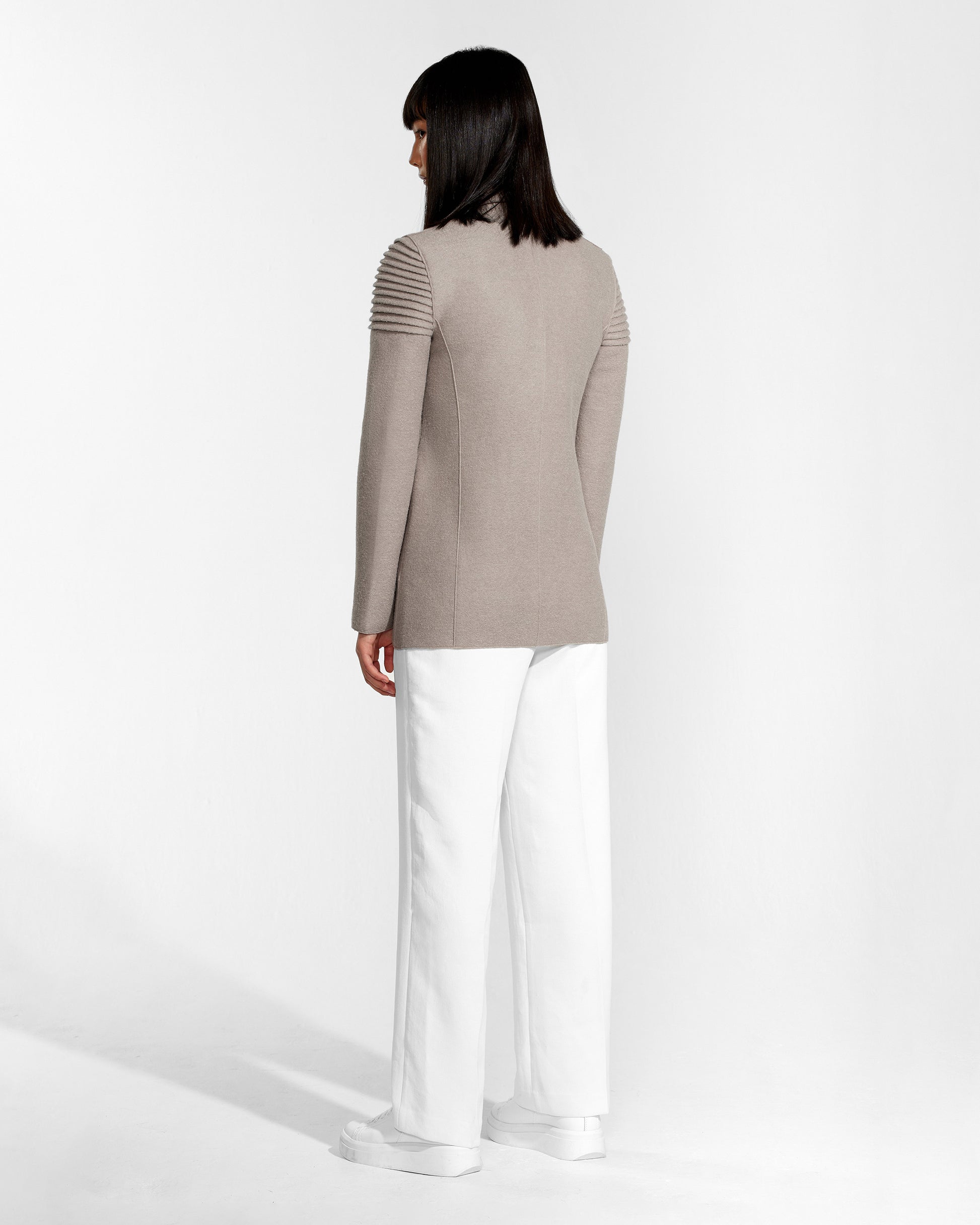 Back view of model wearing a Sentaler double breasted simply taupe blazer made of baby alpaca wool, worn buttoned.