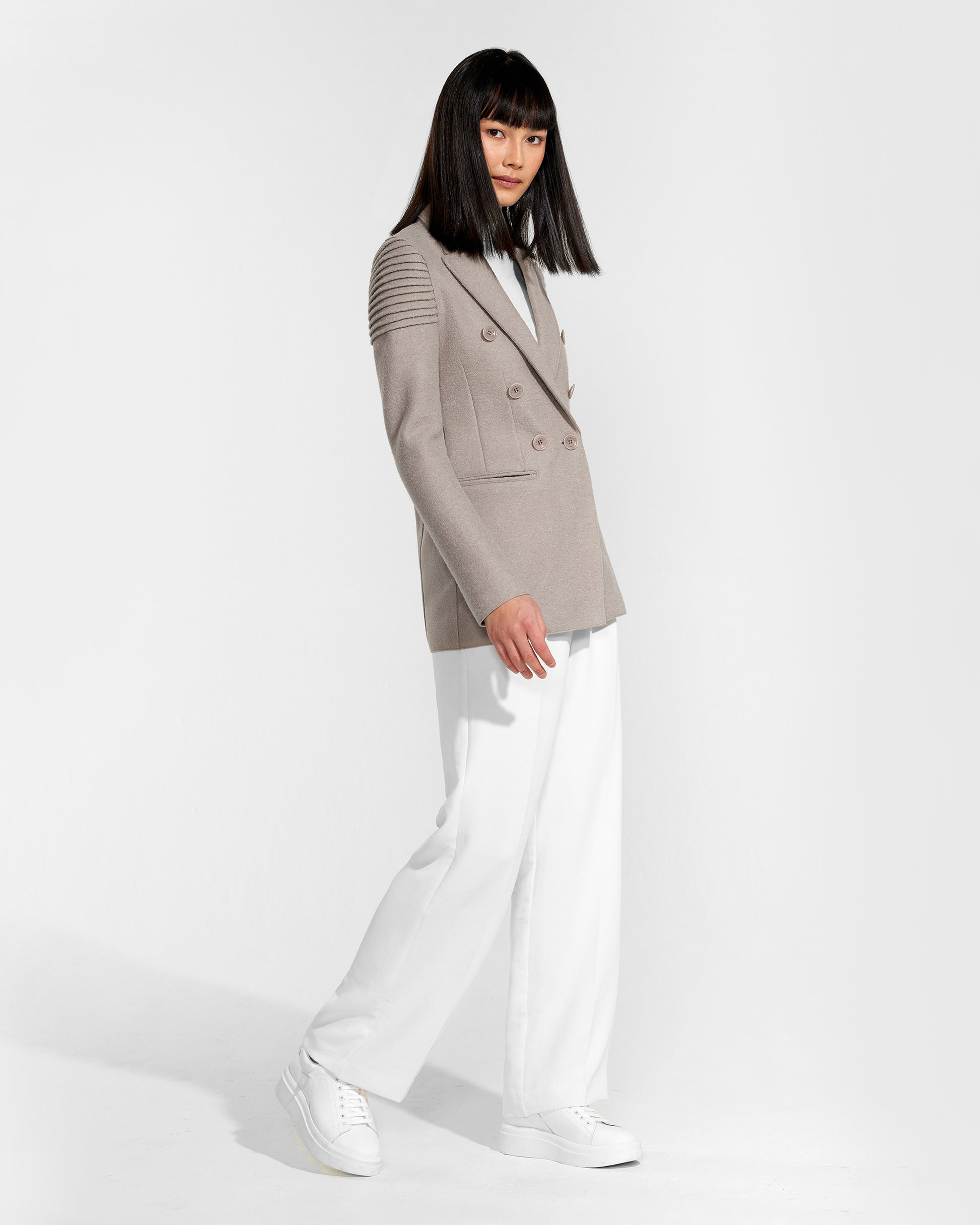 Side view of model wearing a Sentaler double breasted simply taupe blazer made of baby alpaca wool, worn buttoned.