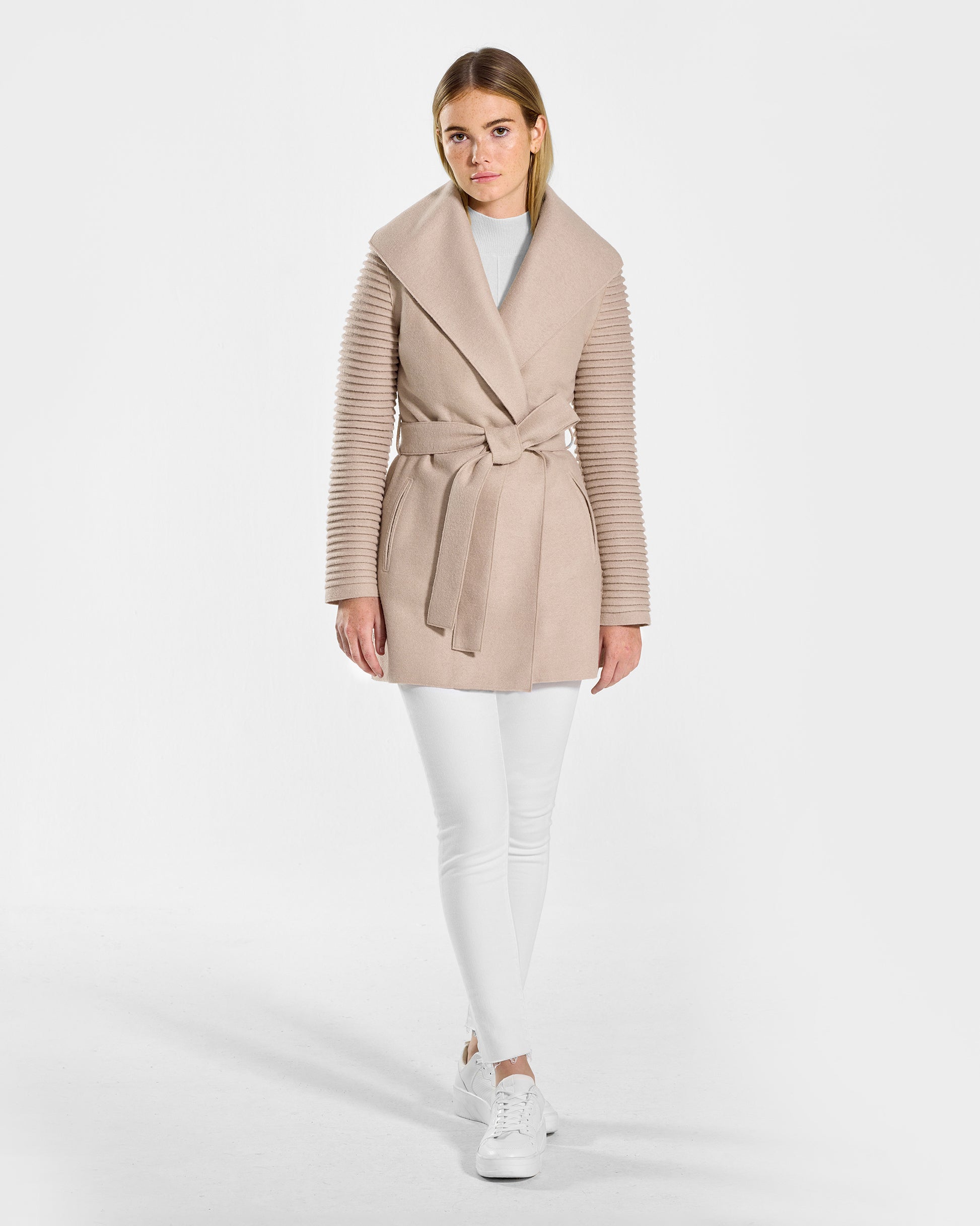 Front view of model wearing a Sentaler chamois beige wrap coat made of superfine alpaca wool, with ribbed sleeves, worn belted.