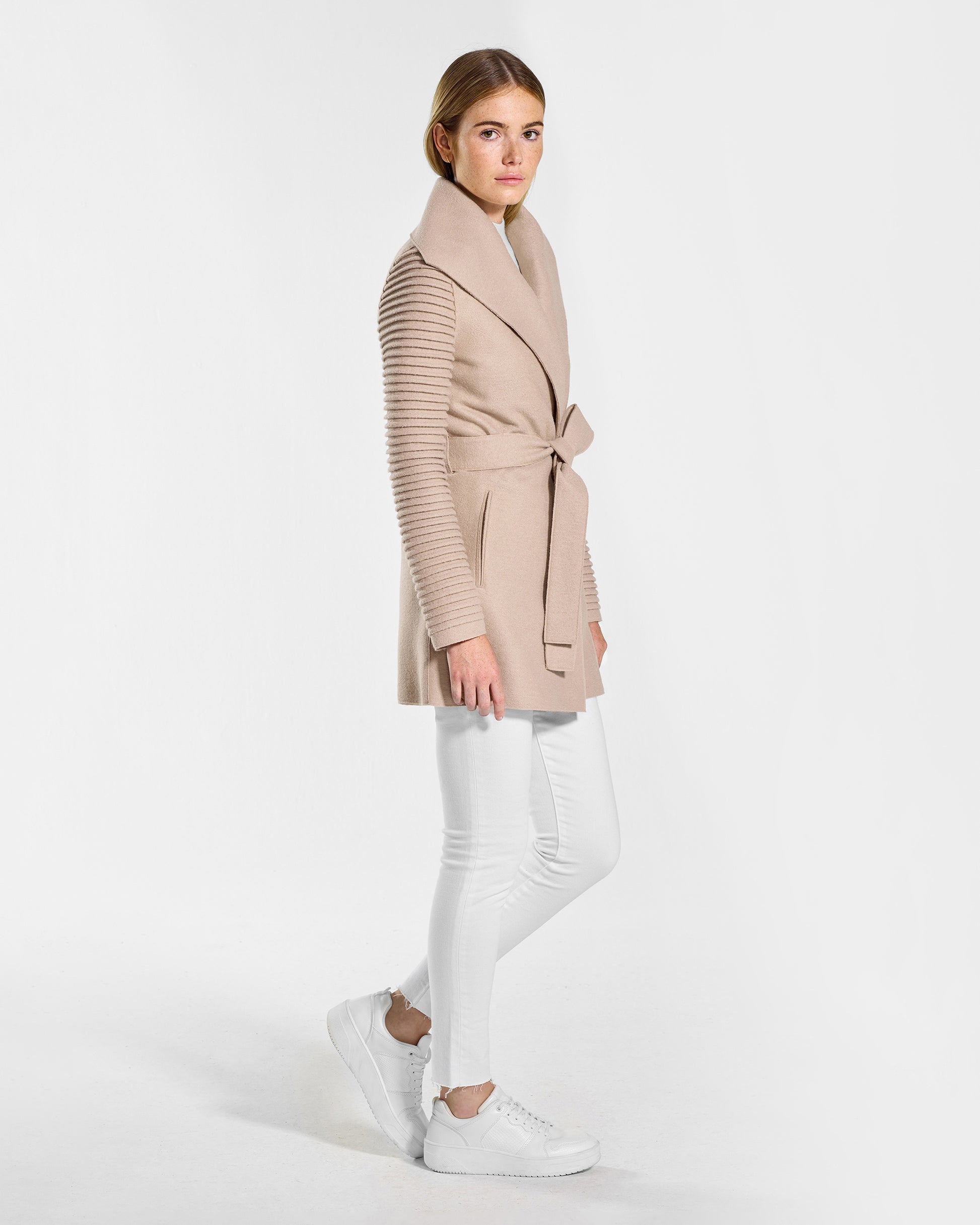 Side view of model wearing a Sentaler chamois beige wrap coat made of superfine alpaca wool, with ribbed sleeves, worn belted.