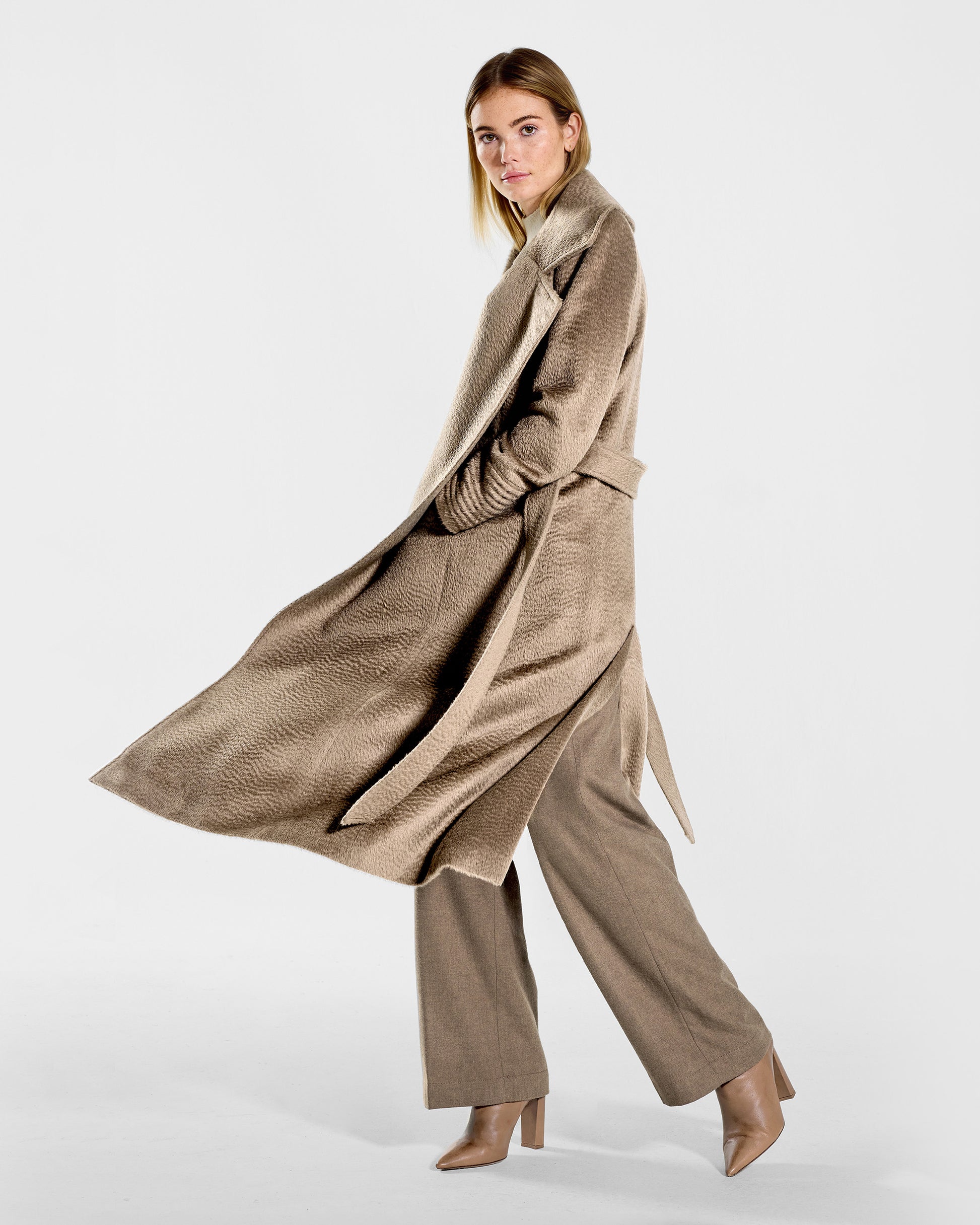 Side view of model wearing a SENTALER long hazelnut brown wrap coat made of suri alpaca wool, with a large notched collar, worn open.