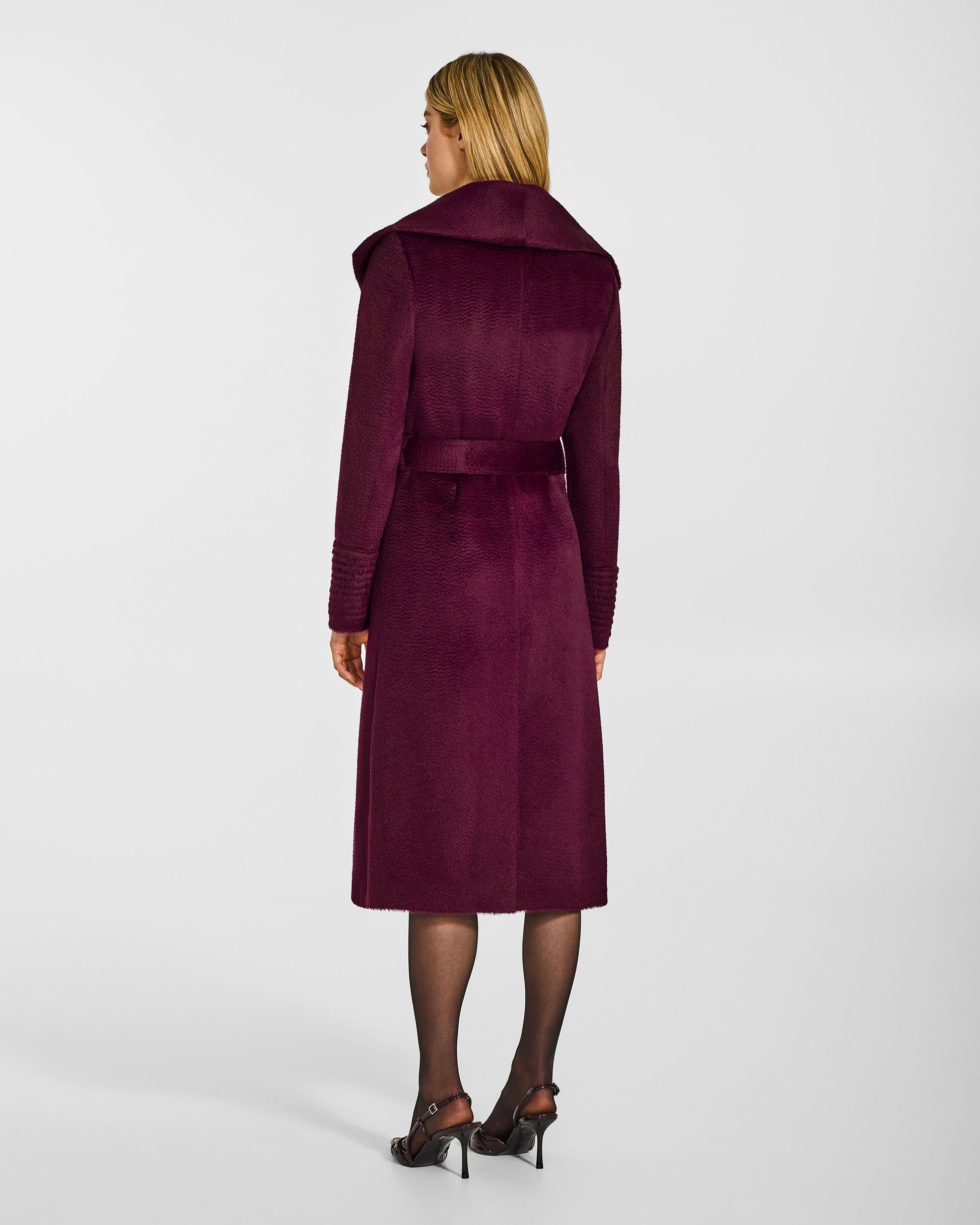 Back view of model wearing a Sentaler long cherry lacquer wrap coat made of suri alpaca wool, with a shawl collar, worn belted.
