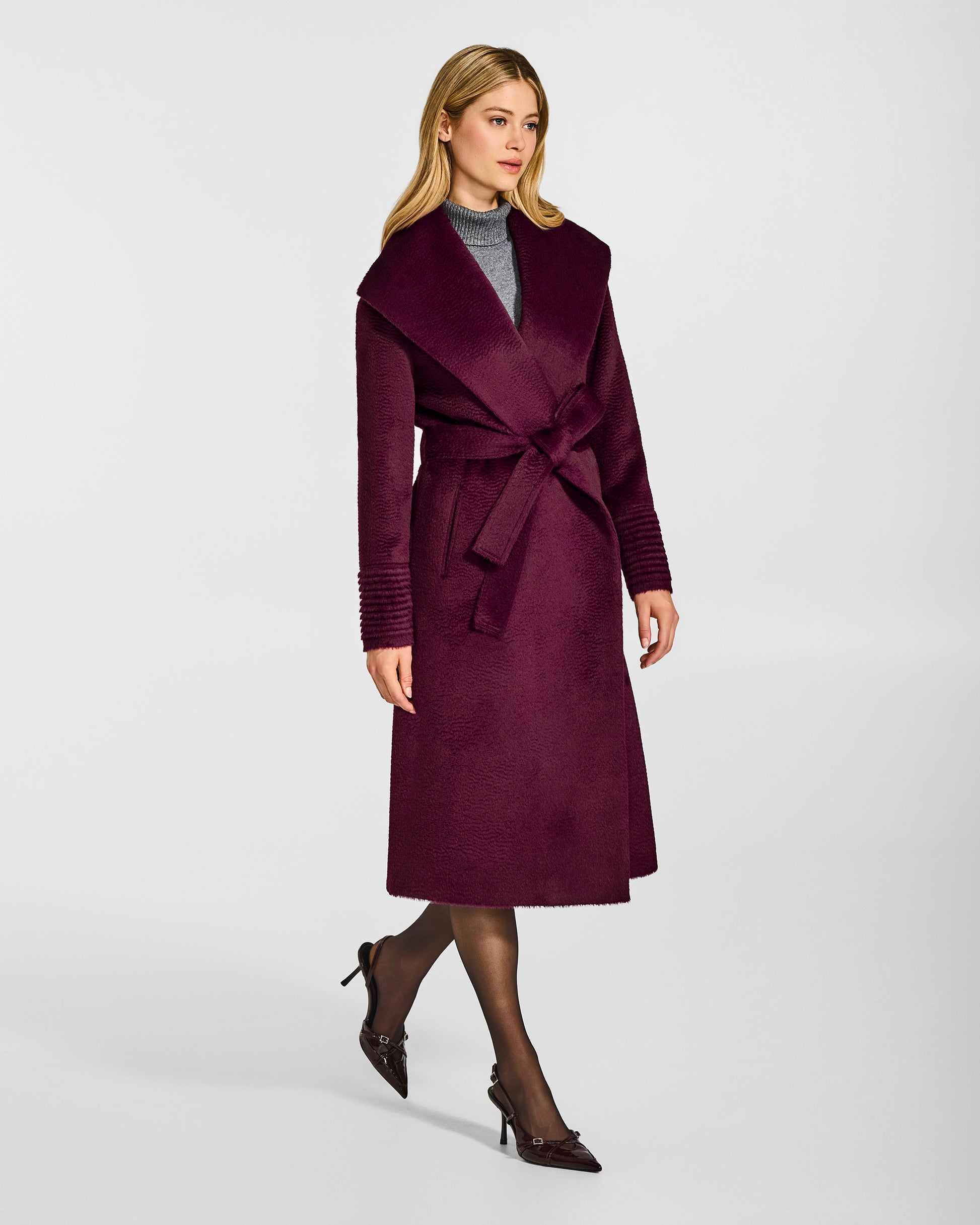 Side view of model wearing a Sentaler long cherry lacquer wrap coat made of suri alpaca wool, with a shawl collar, worn belted.