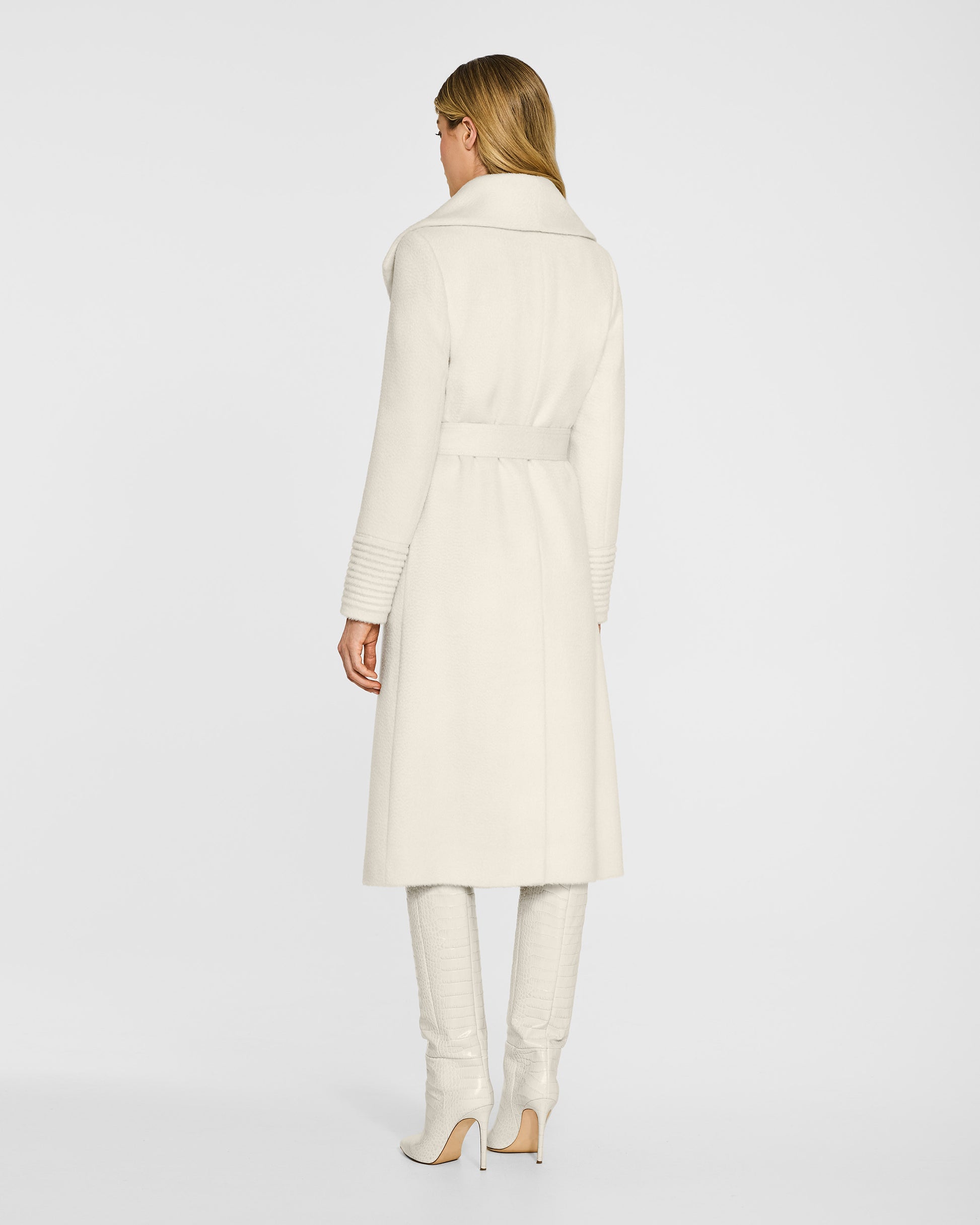 Back view of model wearing a Sentaler long ivory wrap coat made of suri alpaca wool, with a shawl collar, worn belted.
