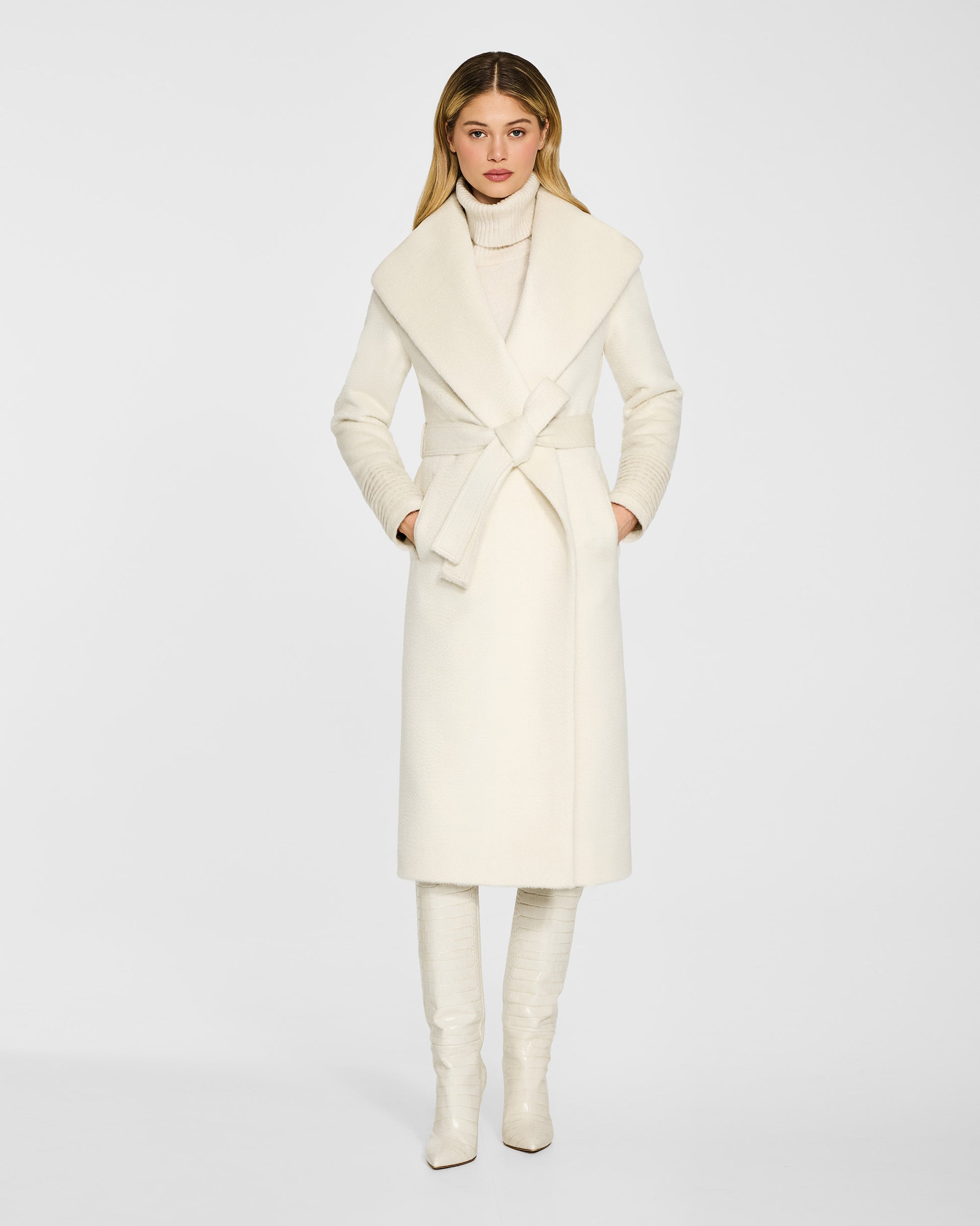 Front view of model wearing a Sentaler long ivory wrap coat made of suri alpaca wool, with a shawl collar, worn belted.