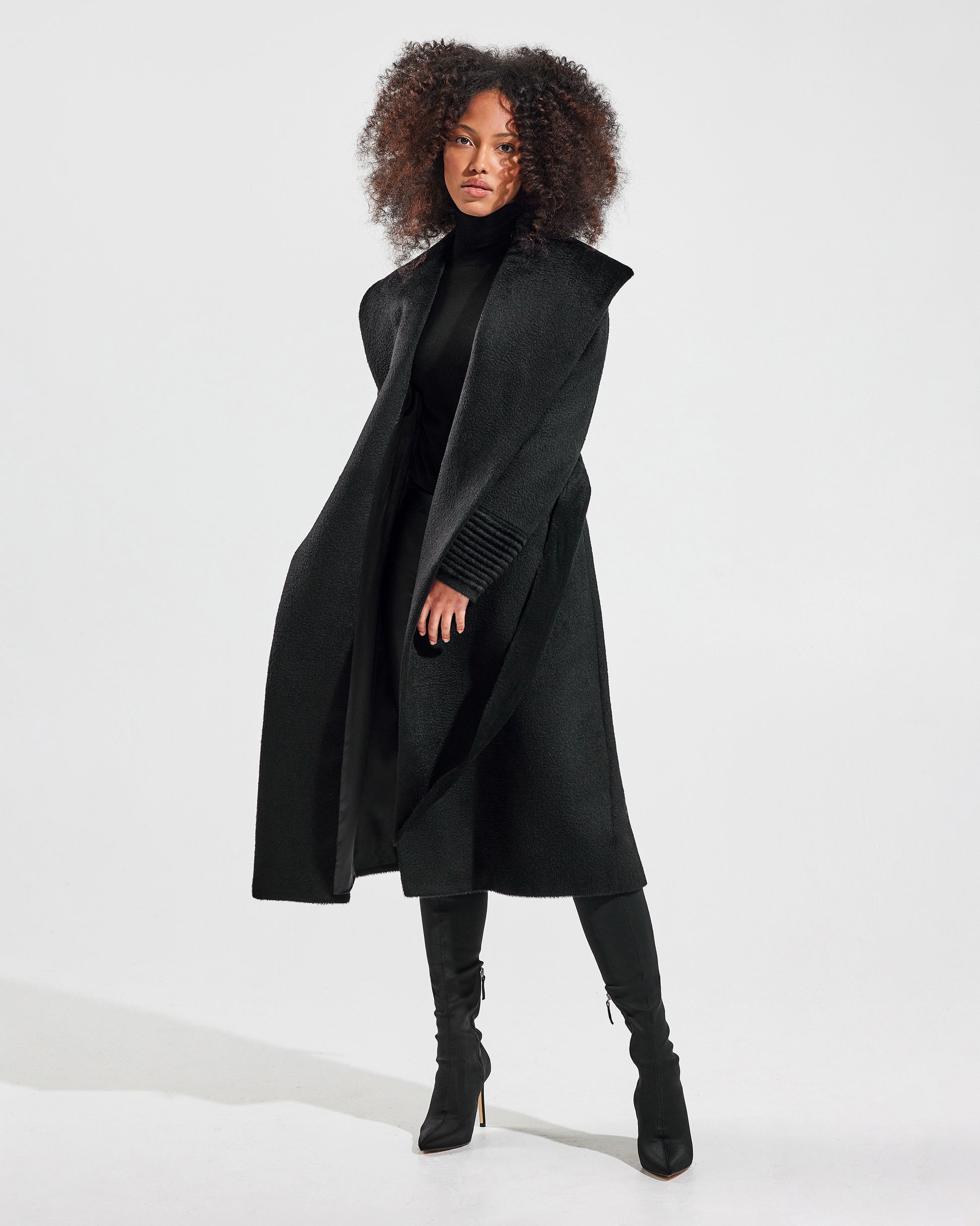 Front view of model wearing a Sentaler long black wrap coat made of suri alpaca wool, with a shawl collar, worn open.