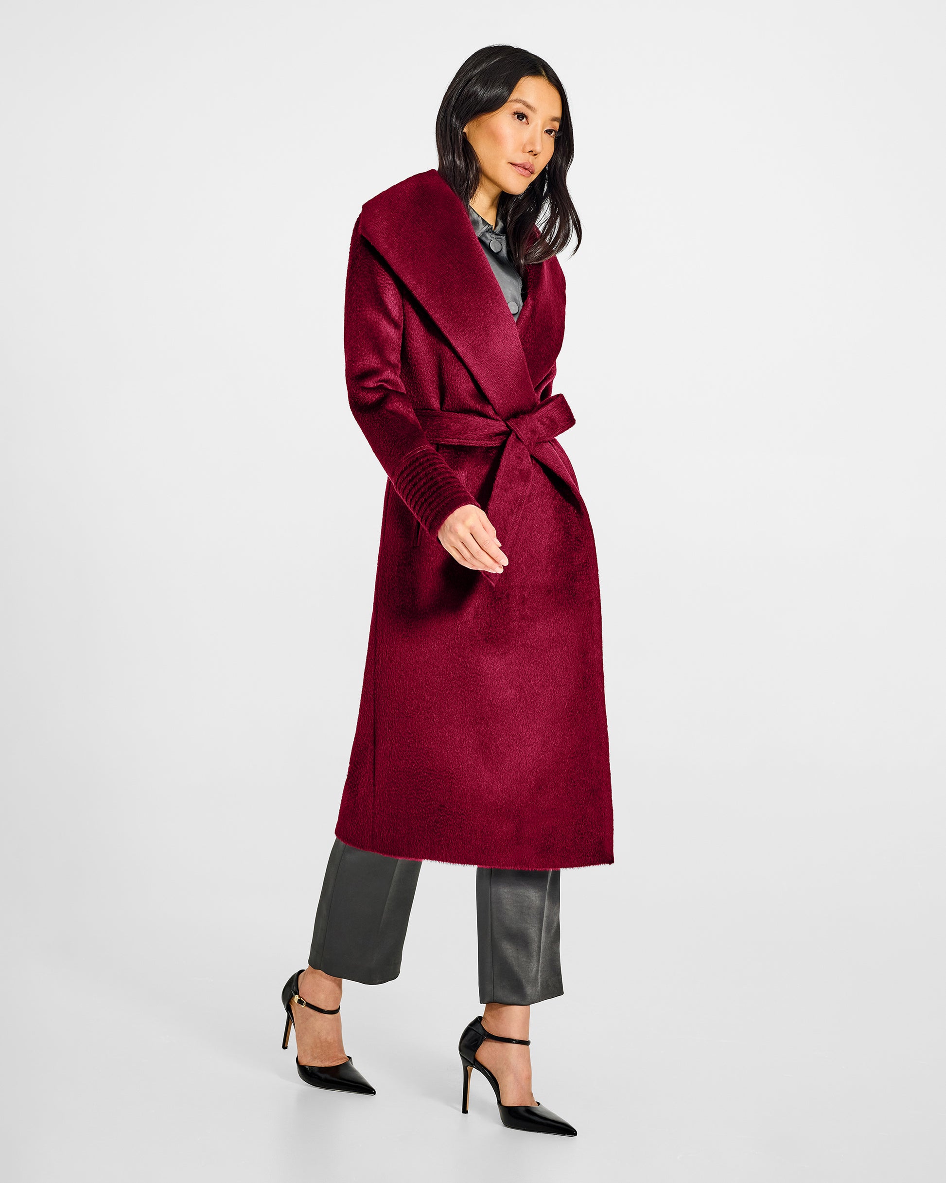 Side view of model wearing a Sentaler long bordeaux wrap coat made of suri alpaca wool, with a shawl collar, worn belted.