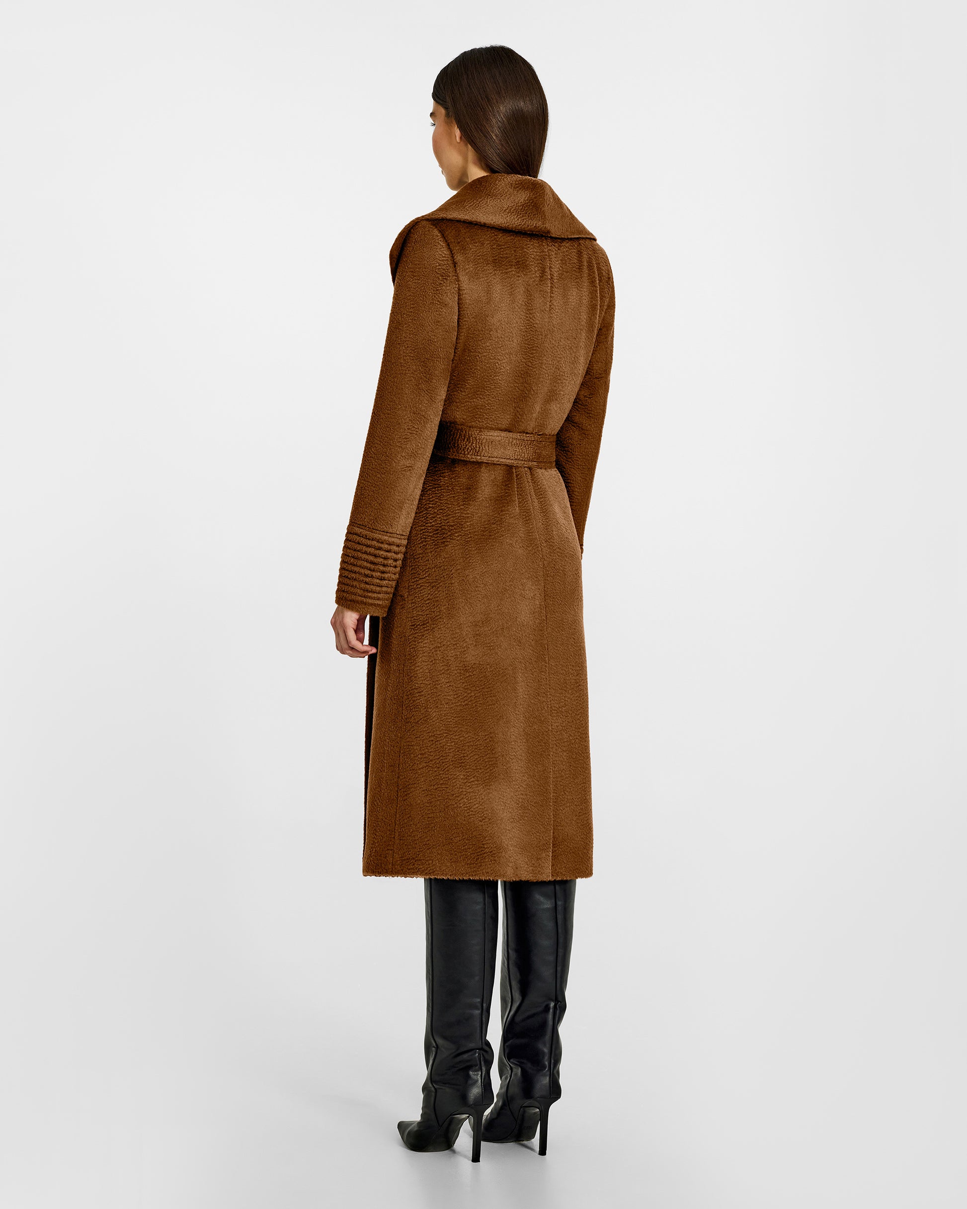 Back view of model wearing a Sentaler long caramel wrap coat made of suri alpaca wool, with a shawl collar, worn belted.