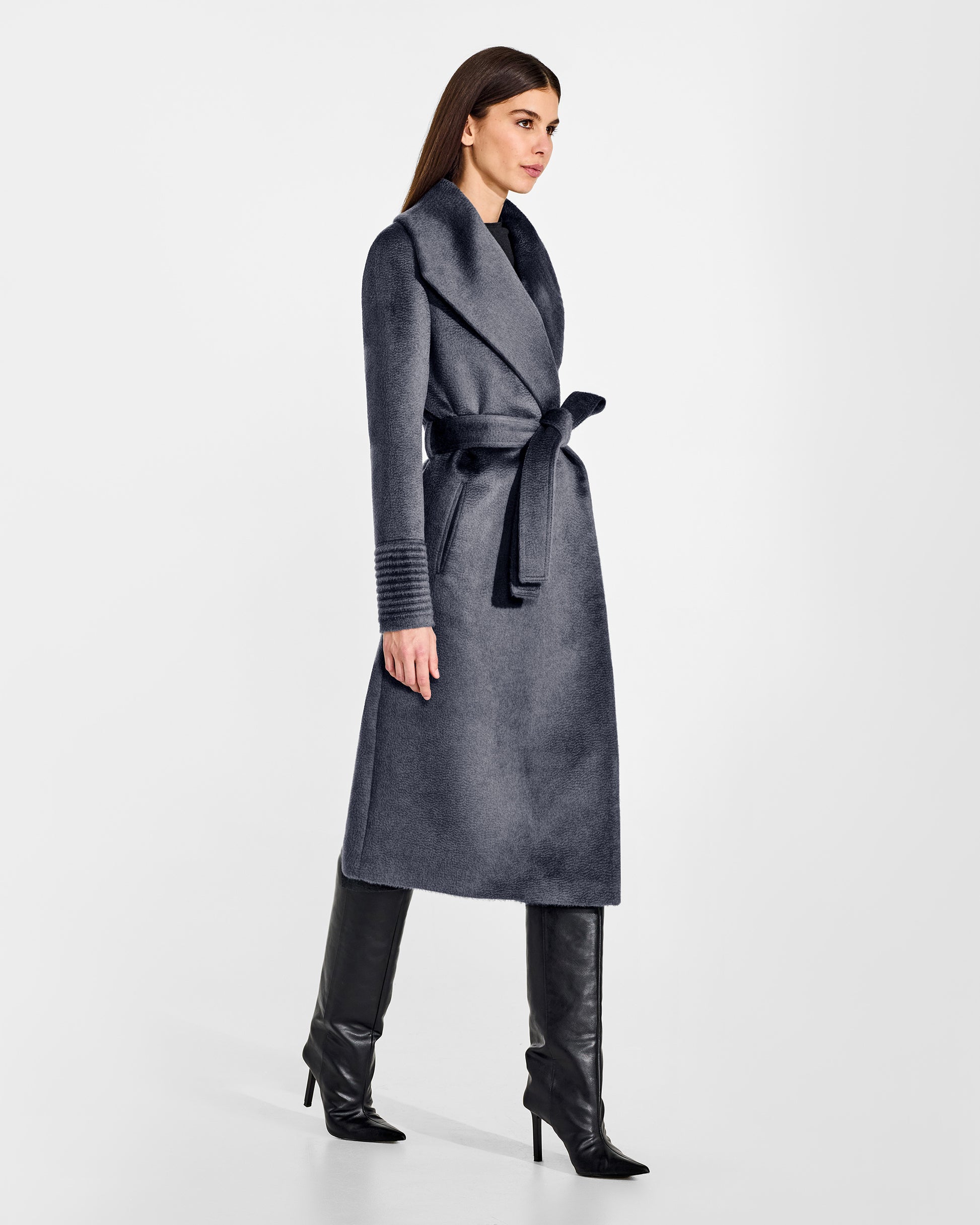 Side view of model wearing a Sentaler long graphite grey wrap coat made of suri alpaca wool, with a shawl collar, worn belted.