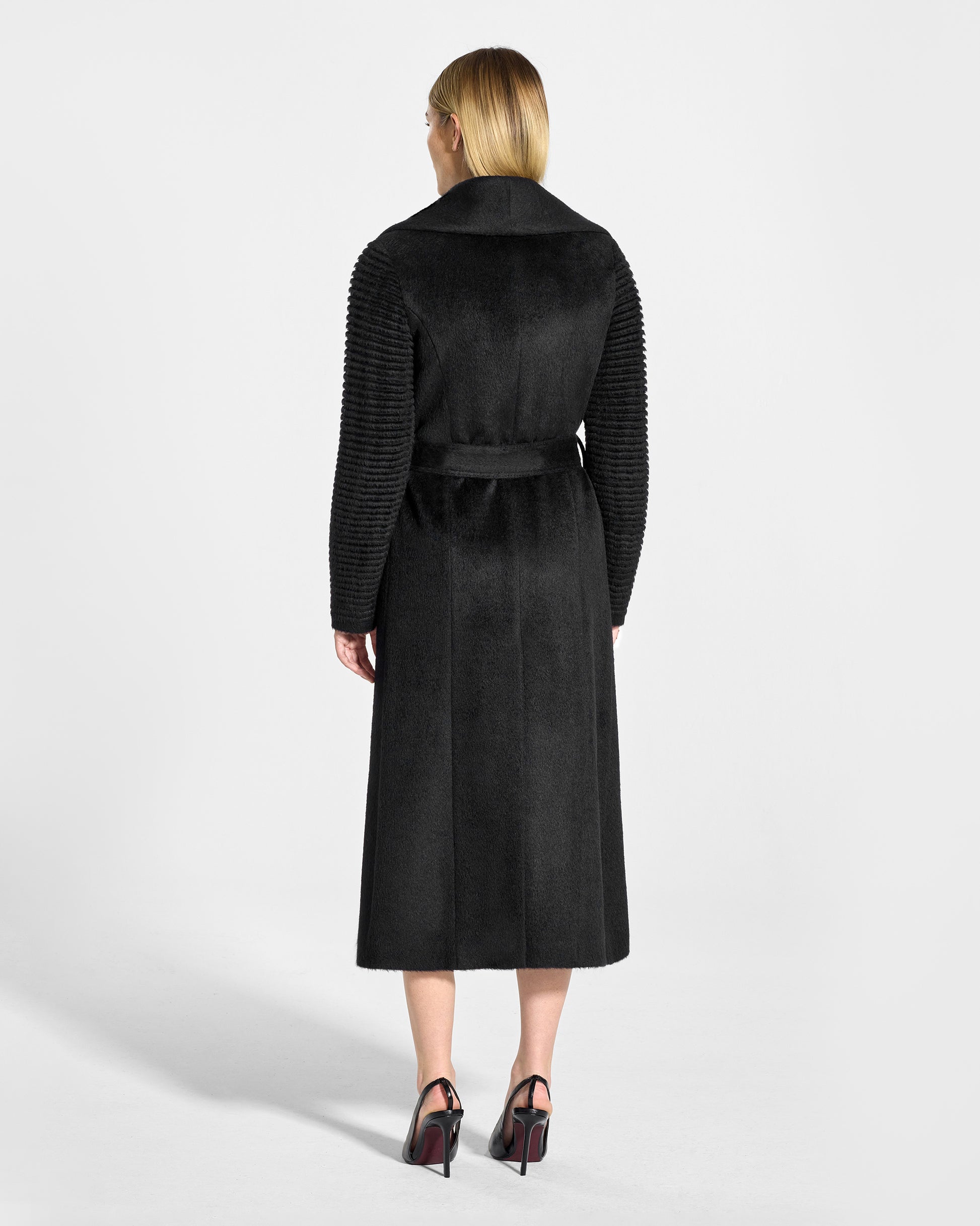 Back view of model wearing a Sentaler long black wrap coat made of suri alpaca wool, with ribbed sleeves, worn belted.