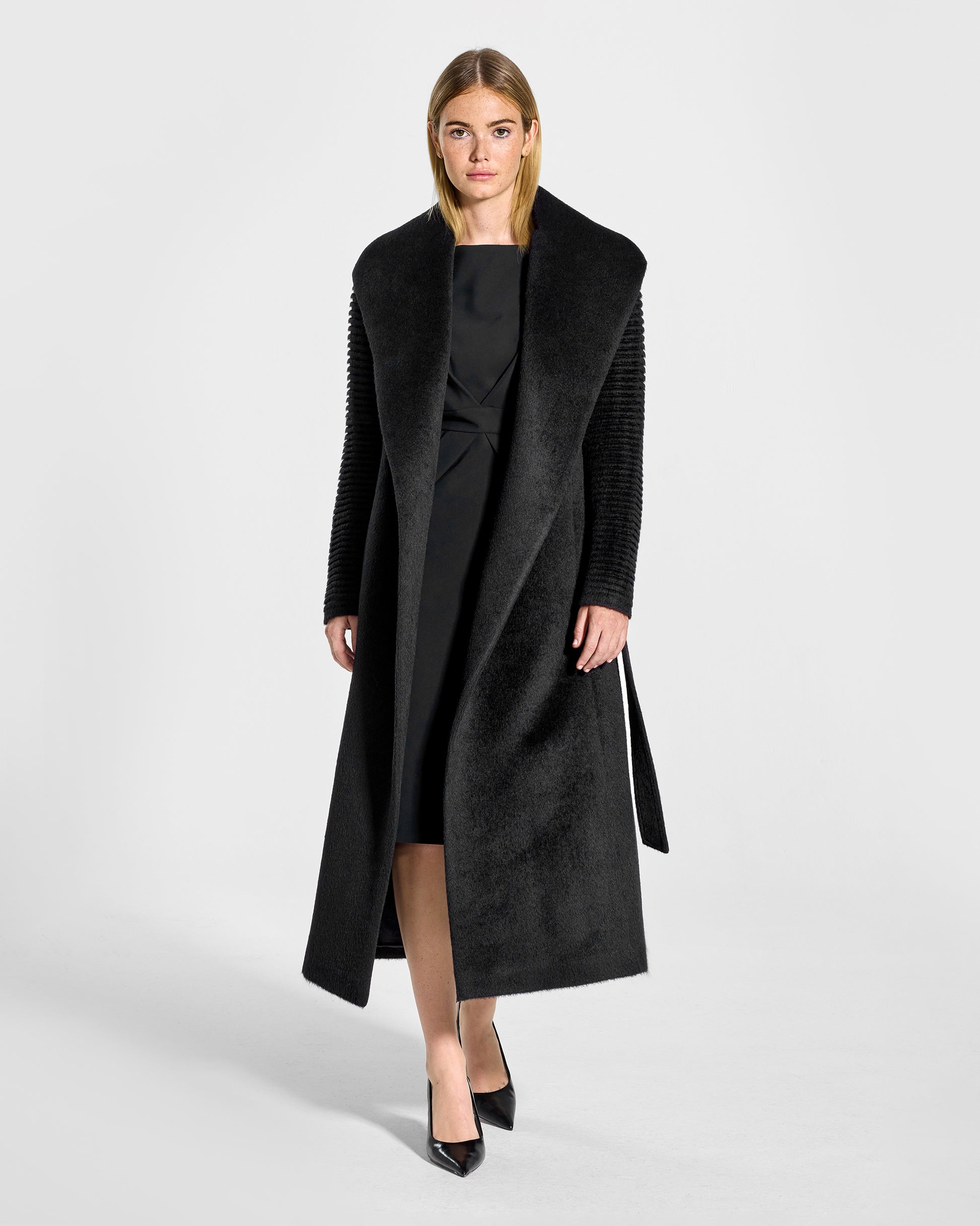 Front view of model wearing a Sentaler long black wrap coat made of suri alpaca wool, with ribbed sleeves, worn open.