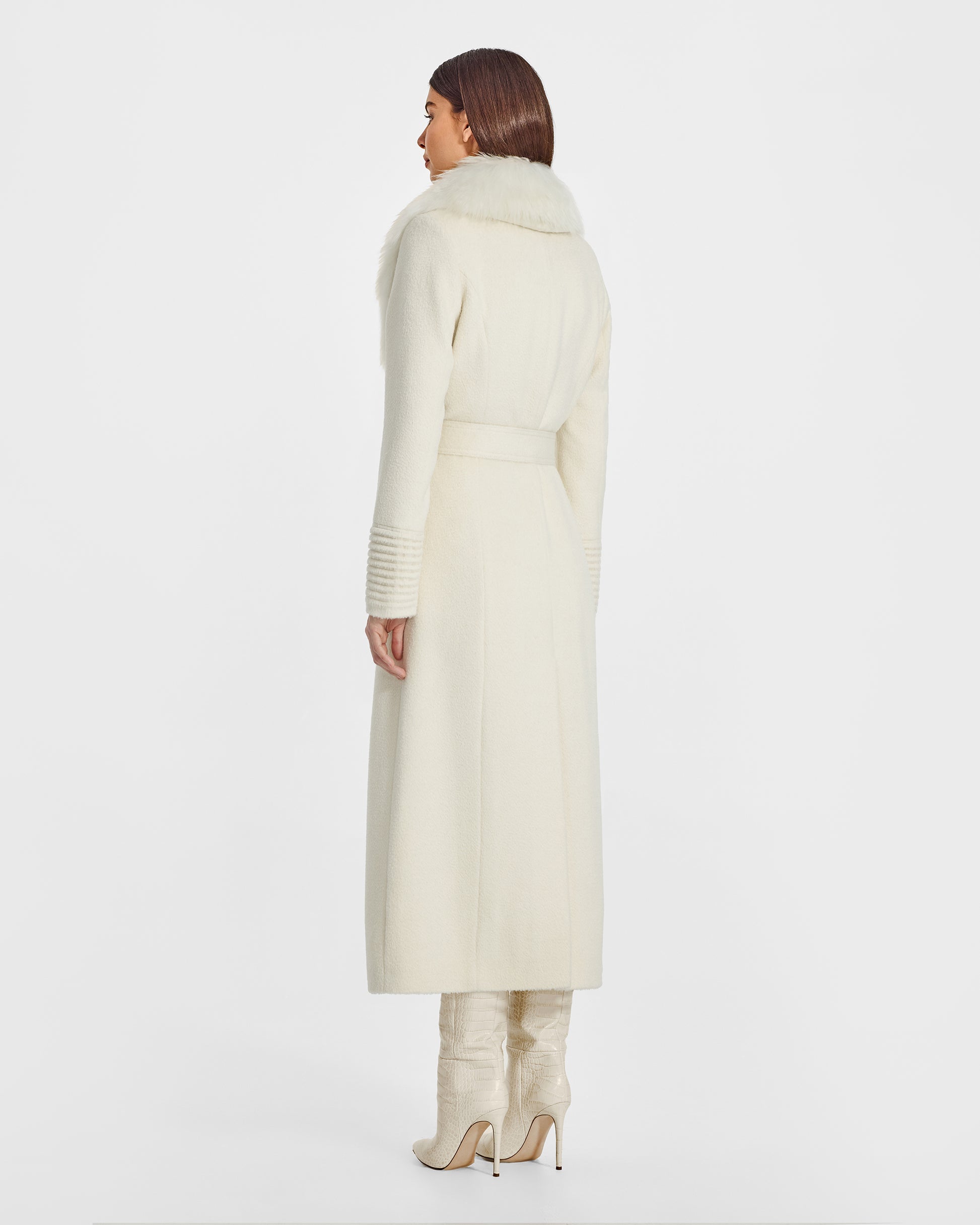 Back view of model wearing a Sentaler ivory maxi coat made of suri alpaca wool, with an alpaca shearling collar, seen belted.