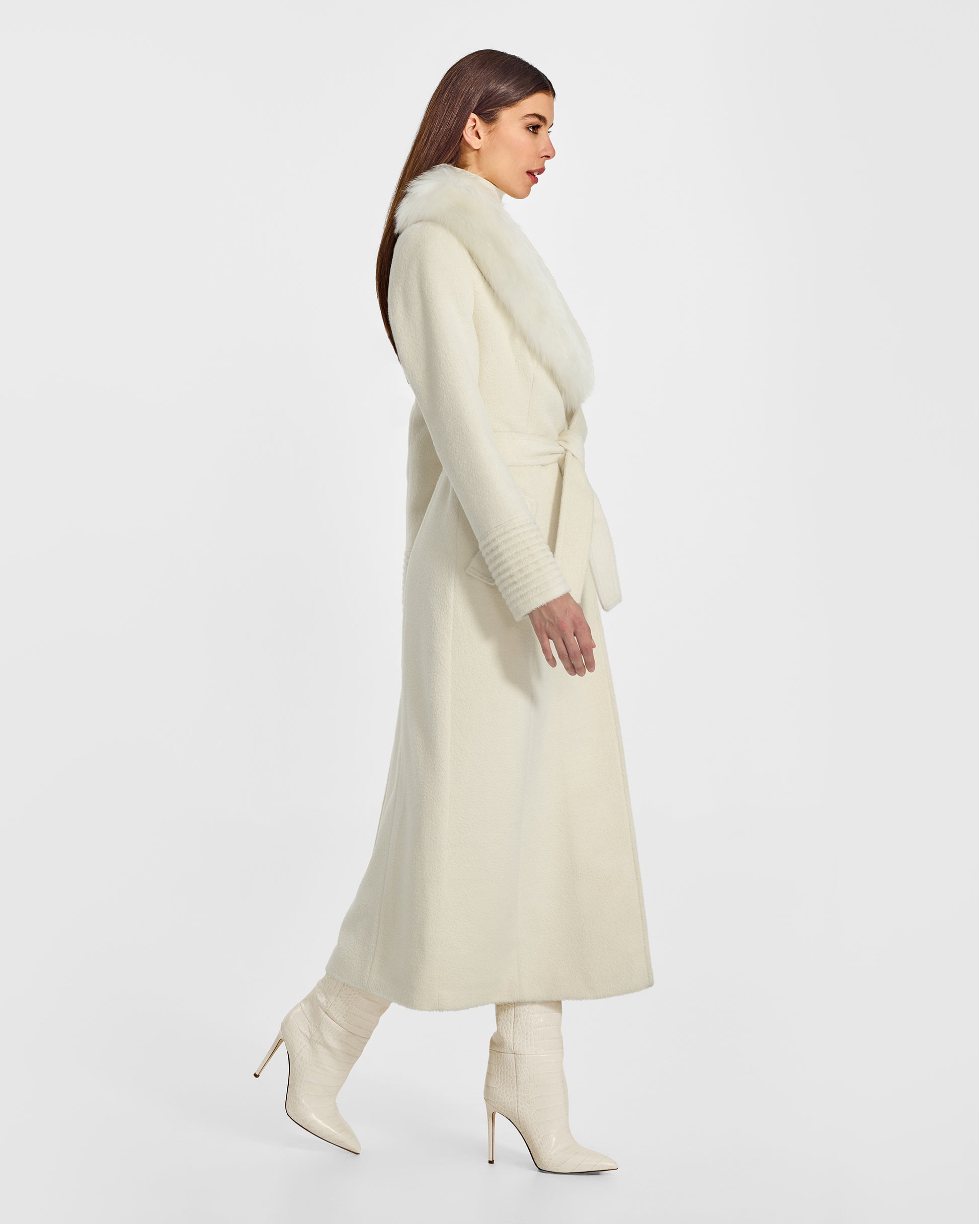 Side view of model wearing a Sentaler ivory maxi coat made of suri alpaca wool, with an alpaca shearling collar, seen belted.