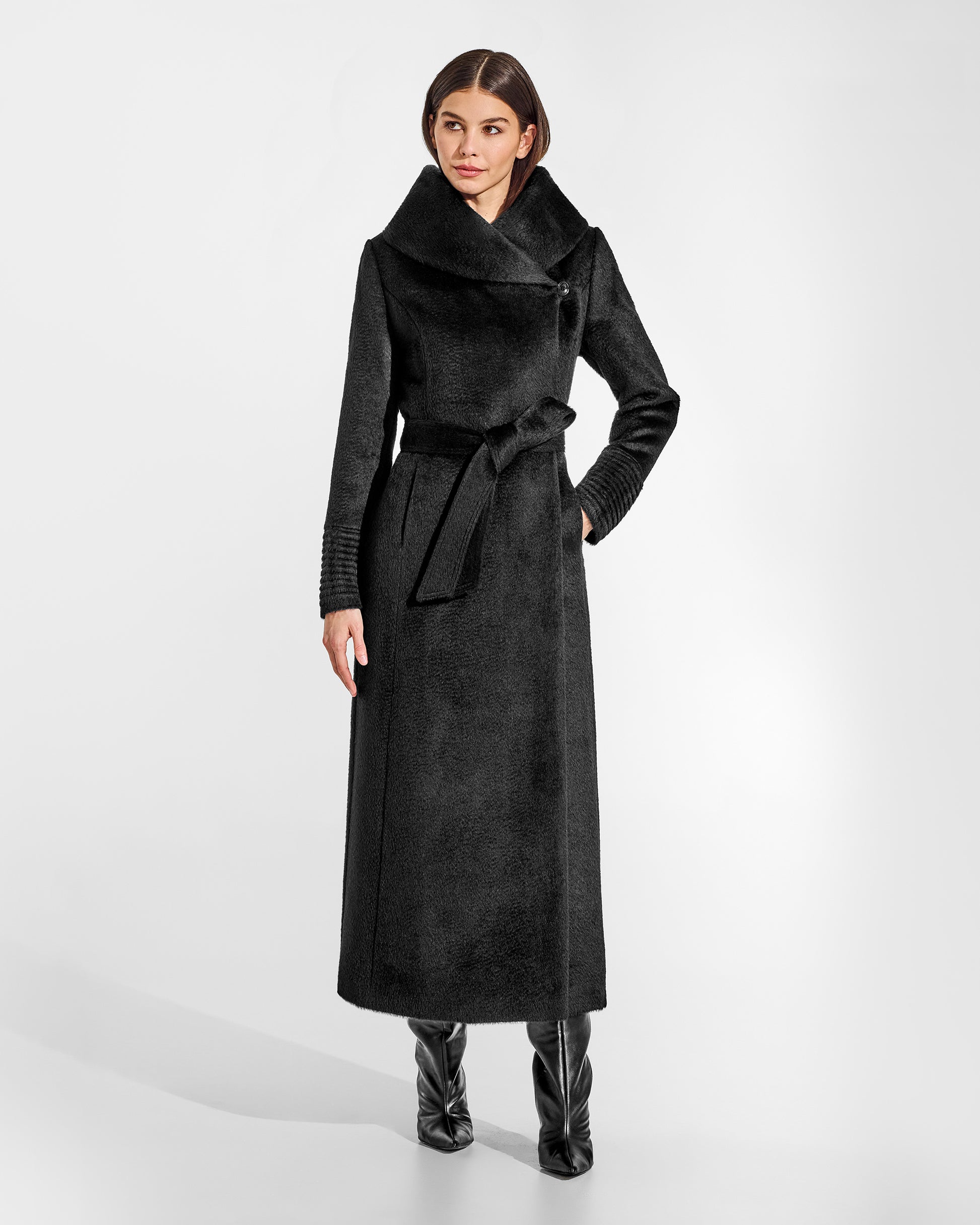 Front view of model wearing a Sentaler maxi black coat made of suri alpaca wool, with a hooded collar, worn belted.