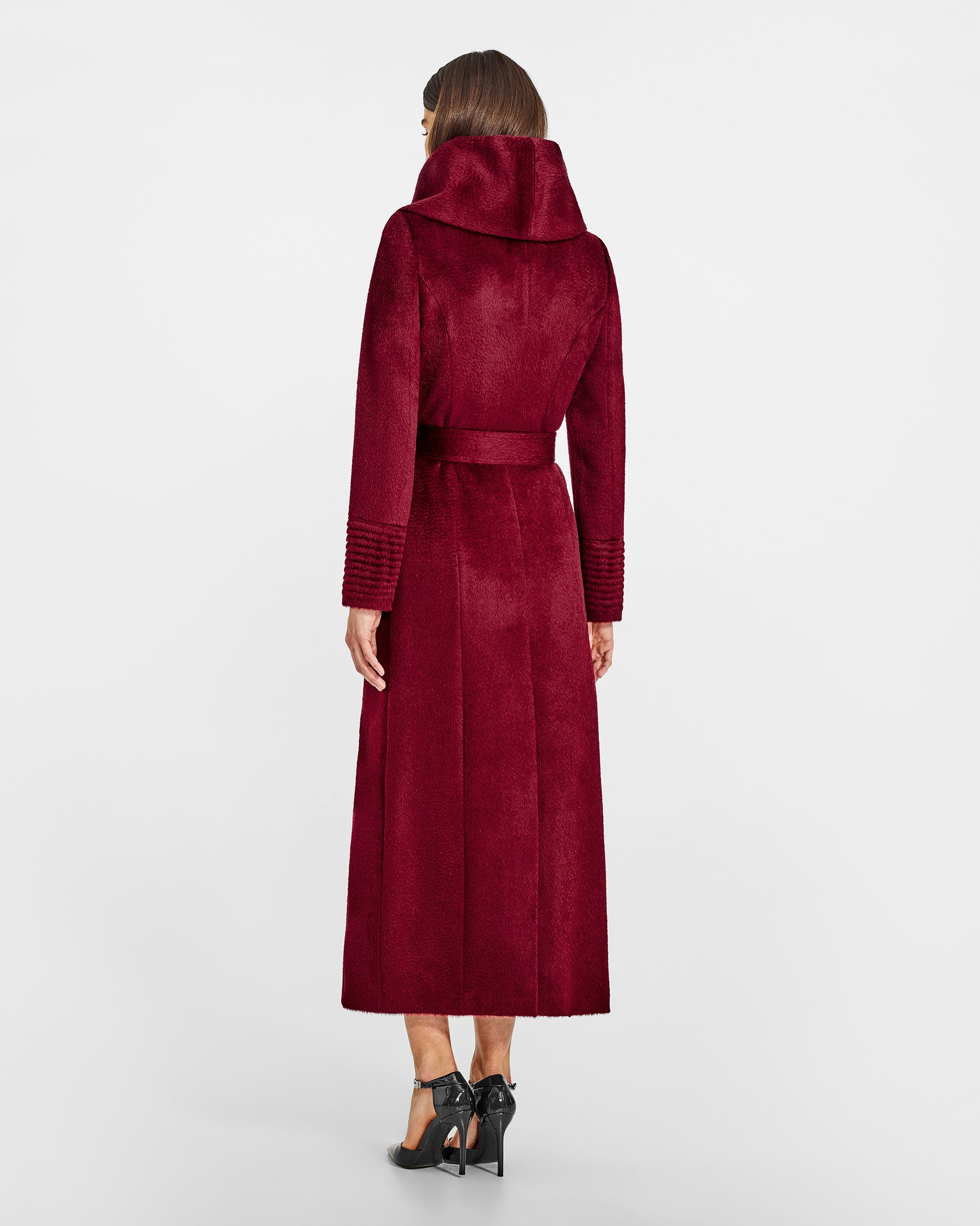 Back view of model wearing a Sentaler maxi bordeaux coat made of suri alpaca wool, with a hooded collar, worn belted.