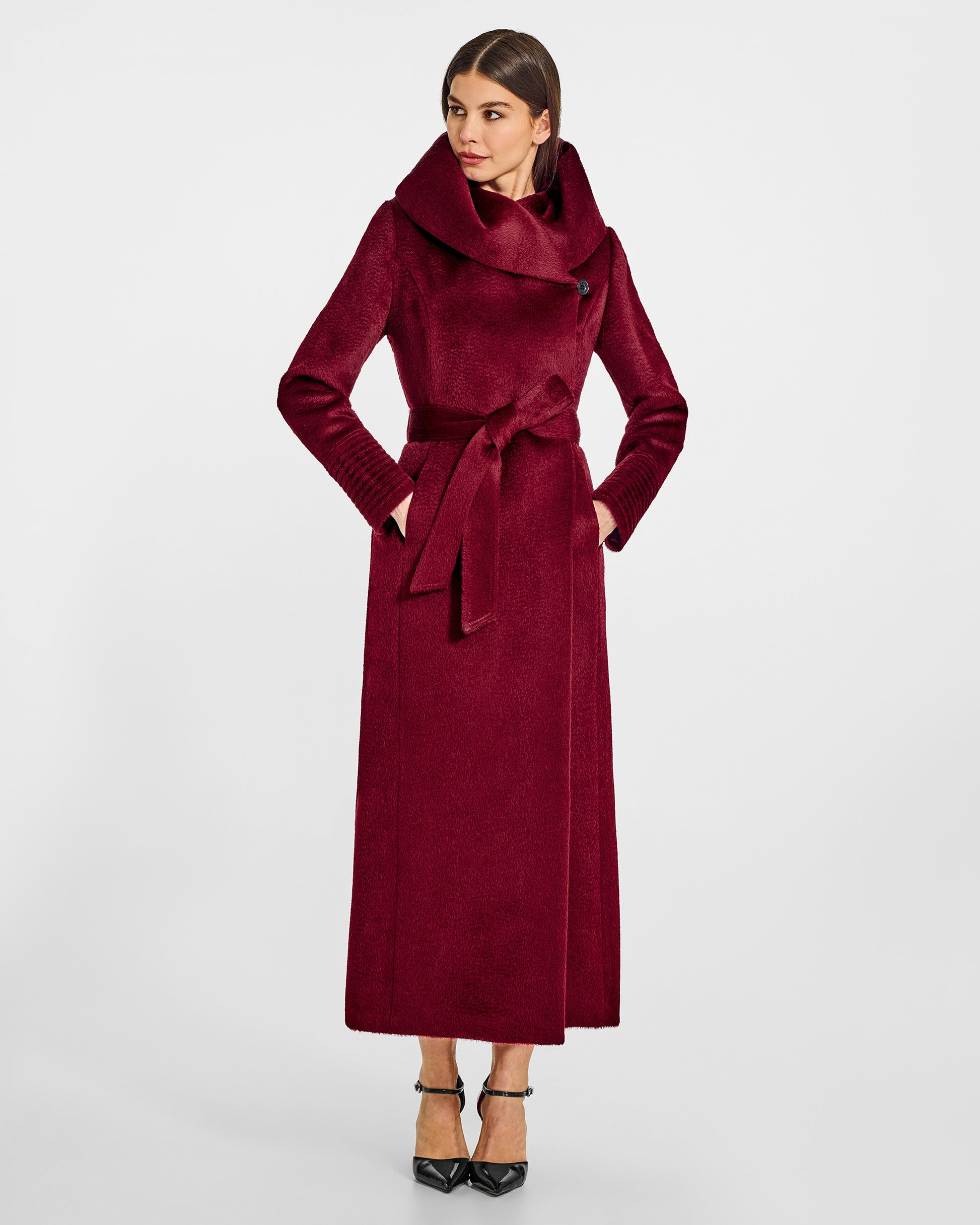 Front view of model wearing a Sentaler maxi bordeaux coat made of suri alpaca wool, with a hooded collar, worn belted.